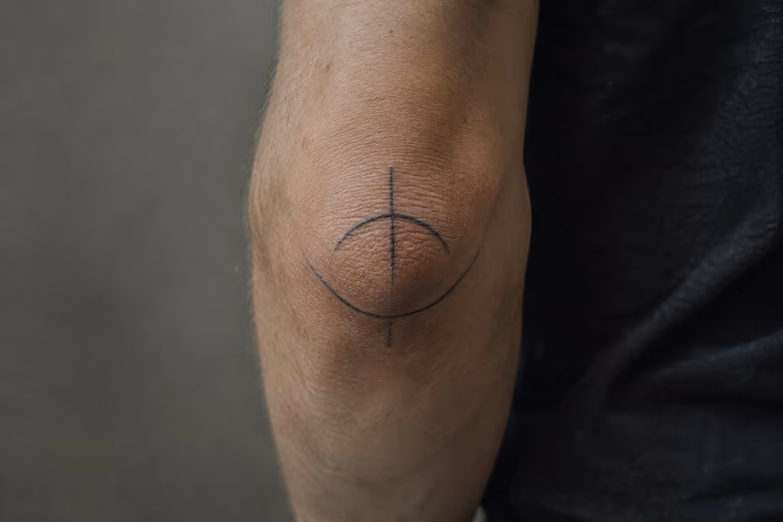 A simple circular tattoo is centered on a person's elbow.