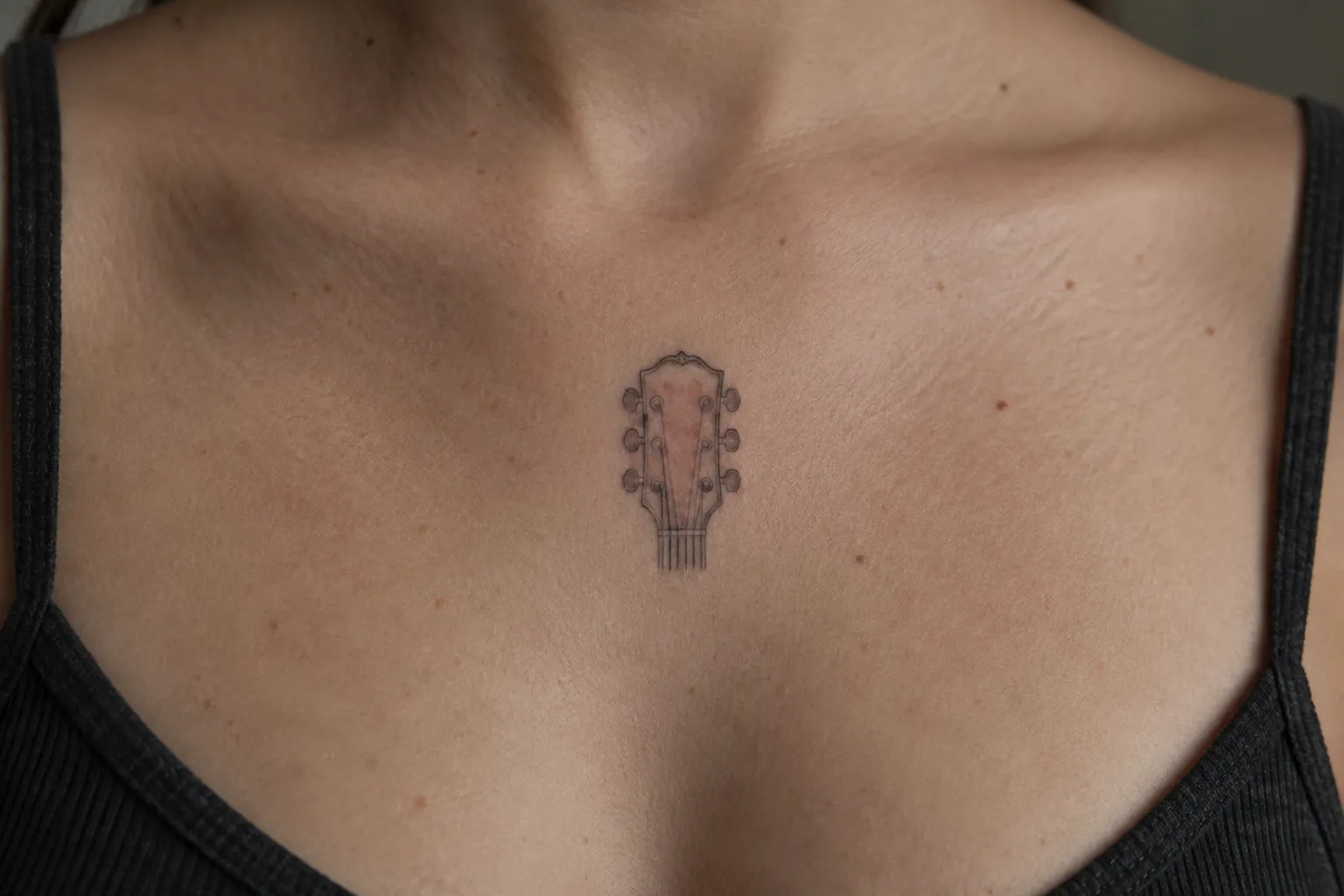 A small guitar-head tattoo sits at the center of a person's upper chest.