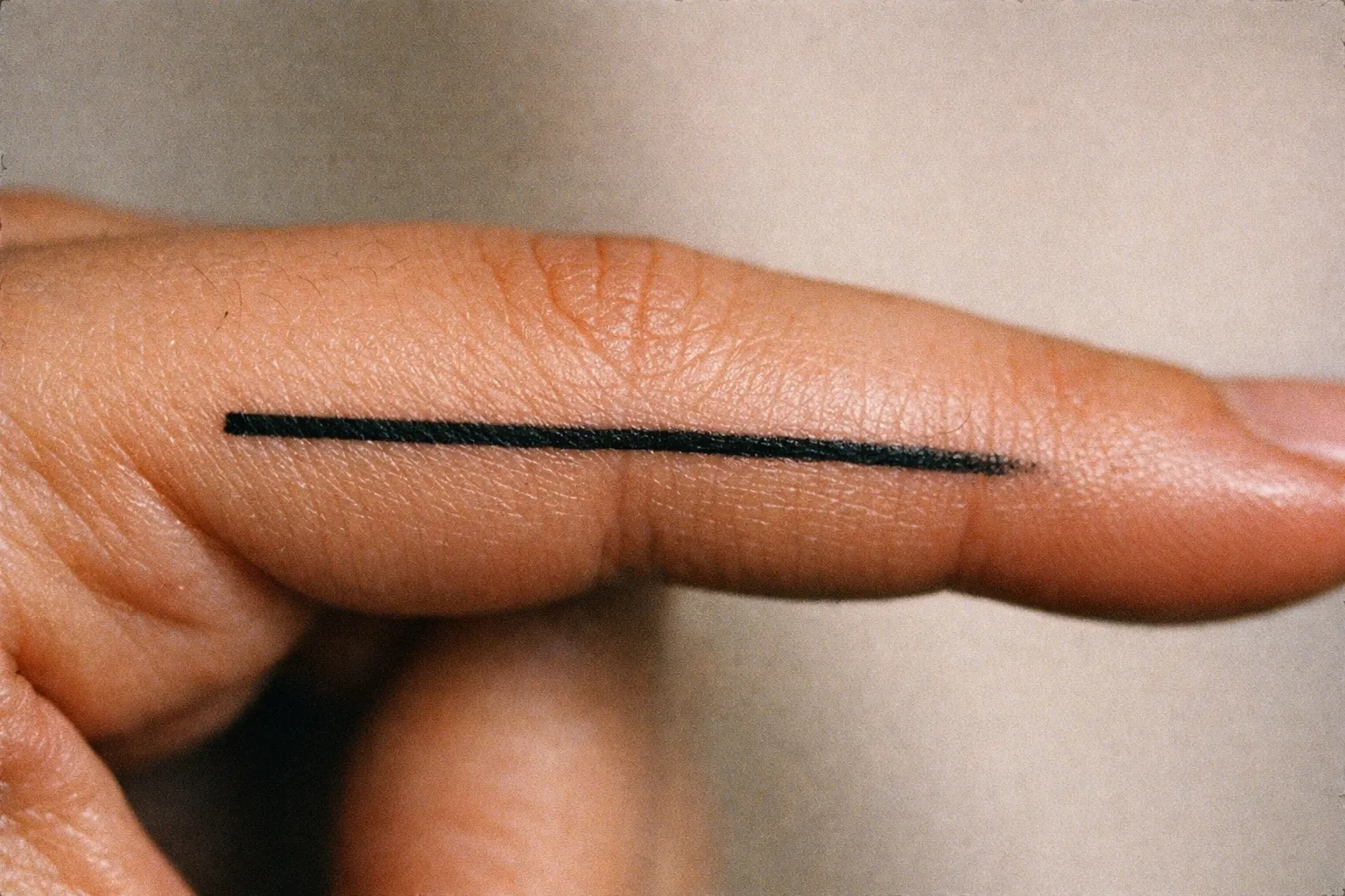 A close-up of a finger with a straight black line tattooed along its side.