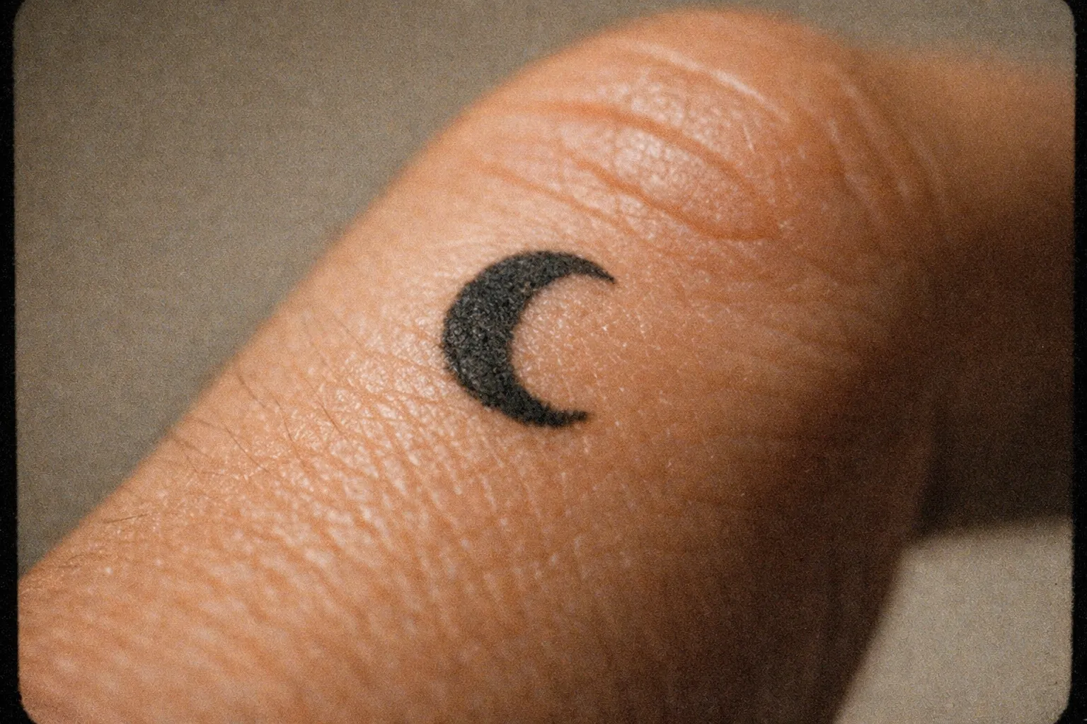 A crescent moon tattoo on the side of a person's finger.