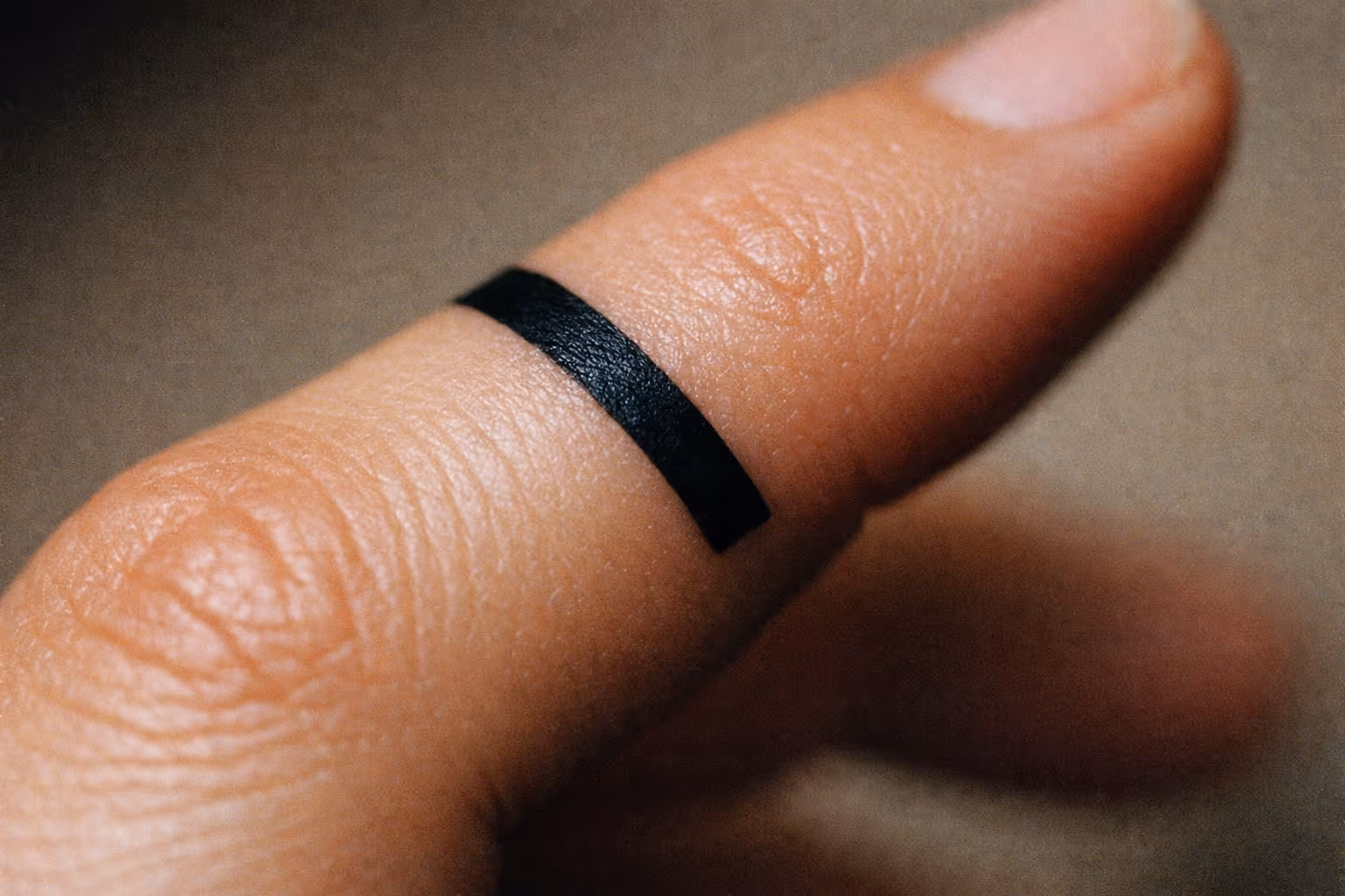 A close-up of a thumb with a solid black band tattooed around it.