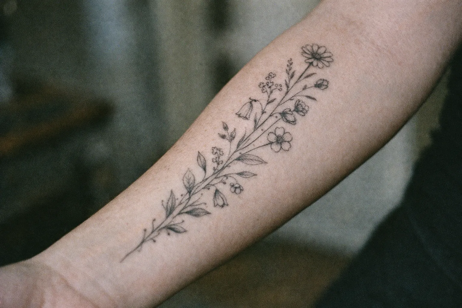 Wildflower bouquet tattoo on forearm with multiple blossoms connected by stems