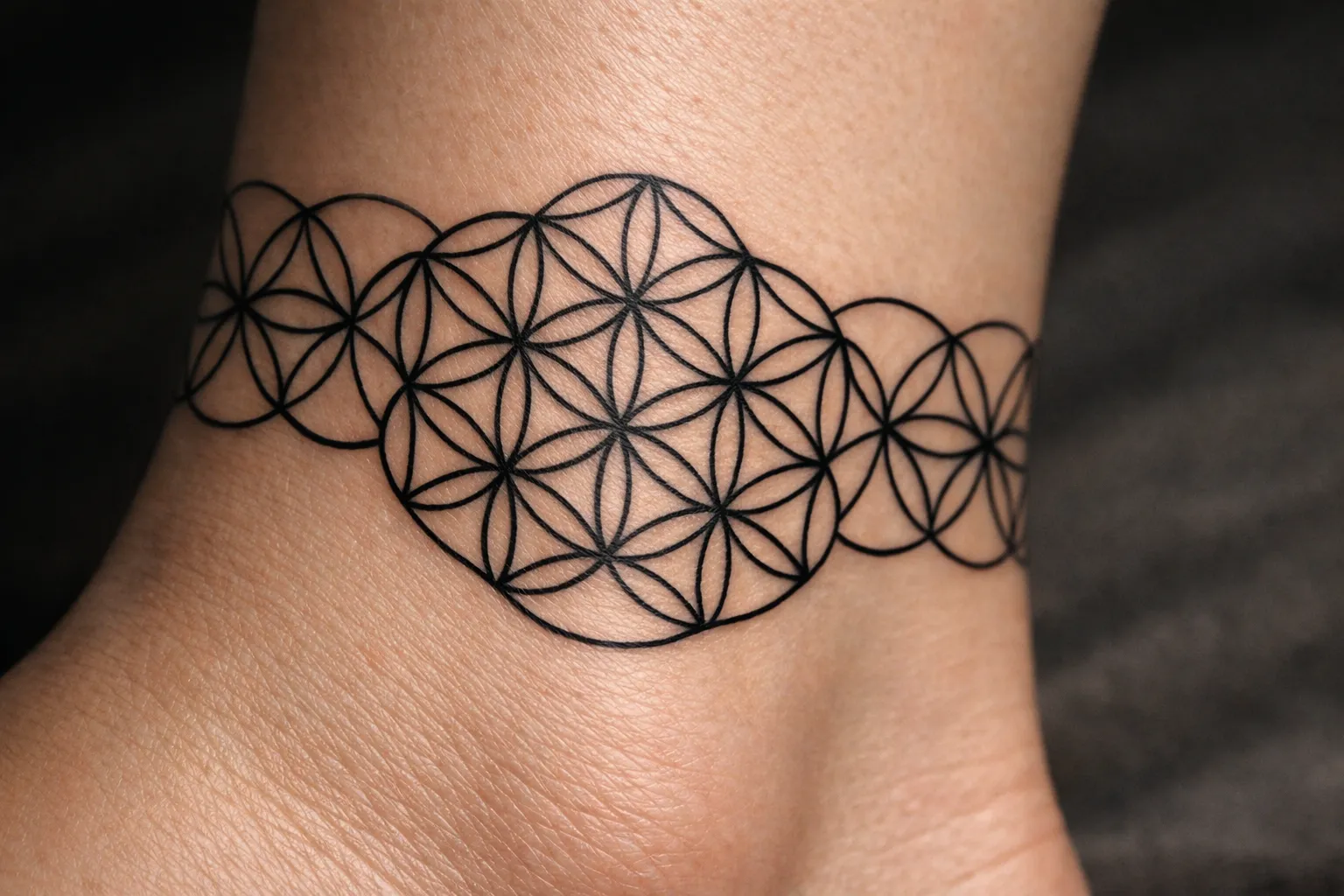 A geometric flower of life tattoo encircles an ankle.