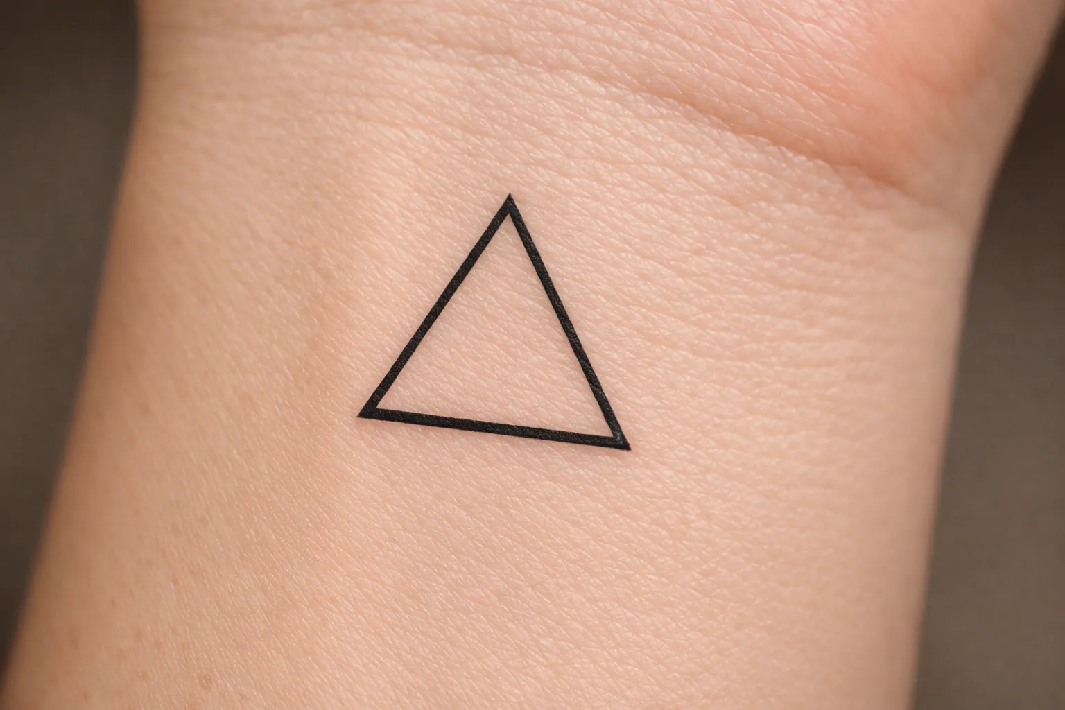 A simple black outline triangle tattoo is on the inside wrist of a person's arm.