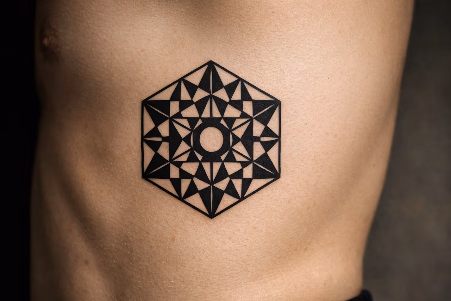 A geometric tattoo with sharp black patterns is inked on the side of a person's torso.