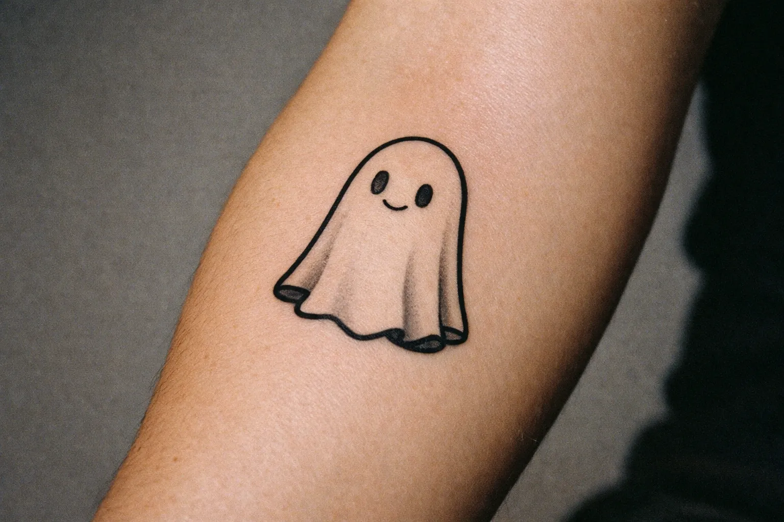Close-up of a minimalist ghost tattoo on inner forearm, black linework