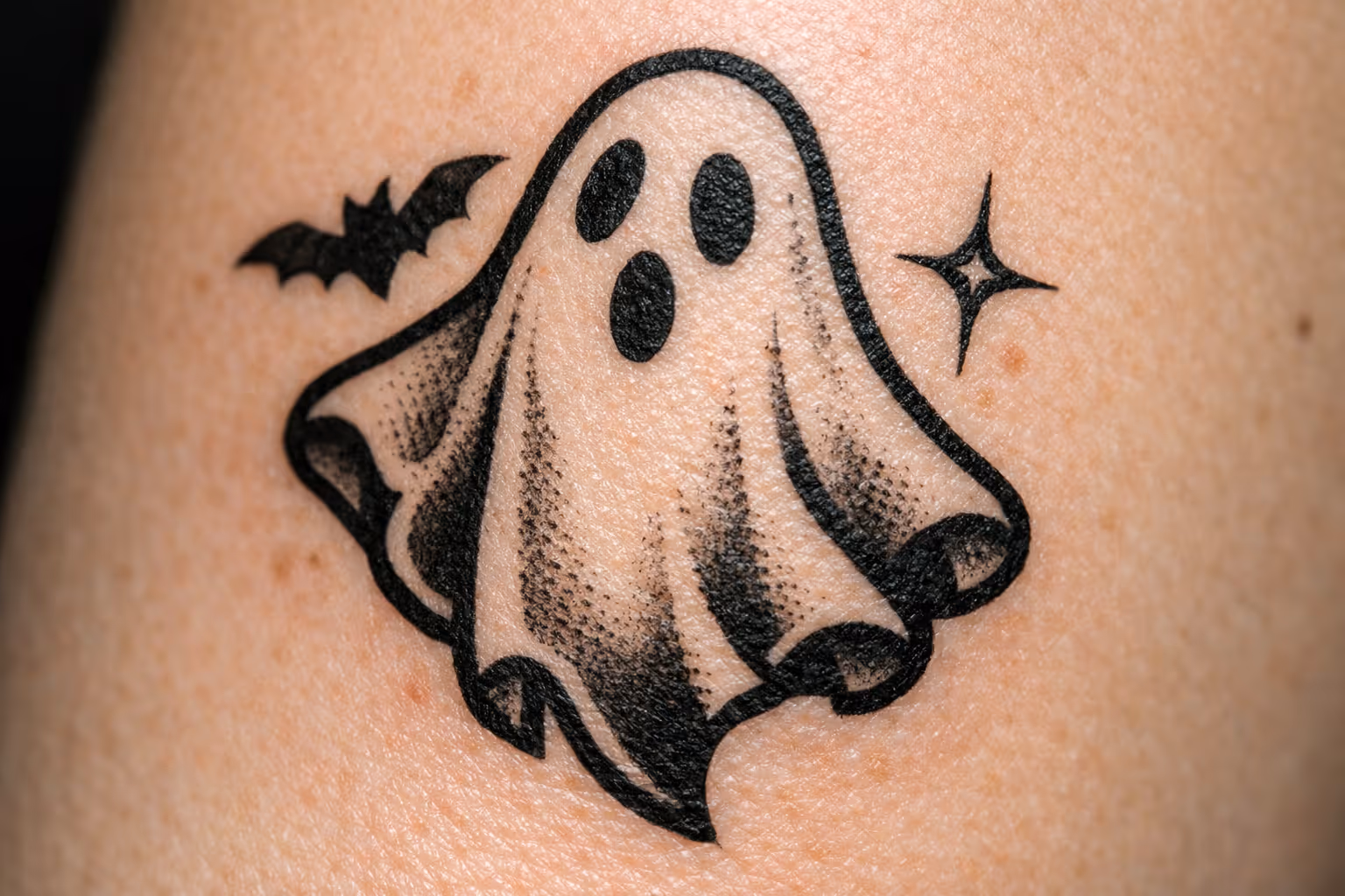 A cartoon ghost tattoo on skin with a small bat and star beside it.