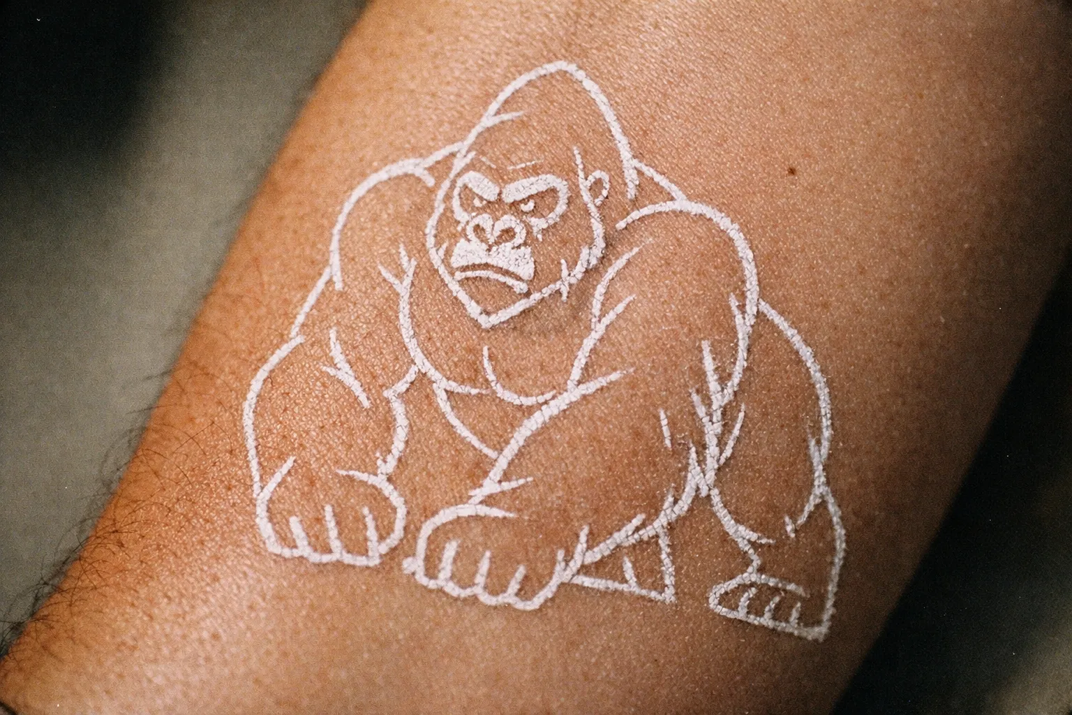 Forearm close-up showing chalk stencil outline of a gorilla tattoo on the skin