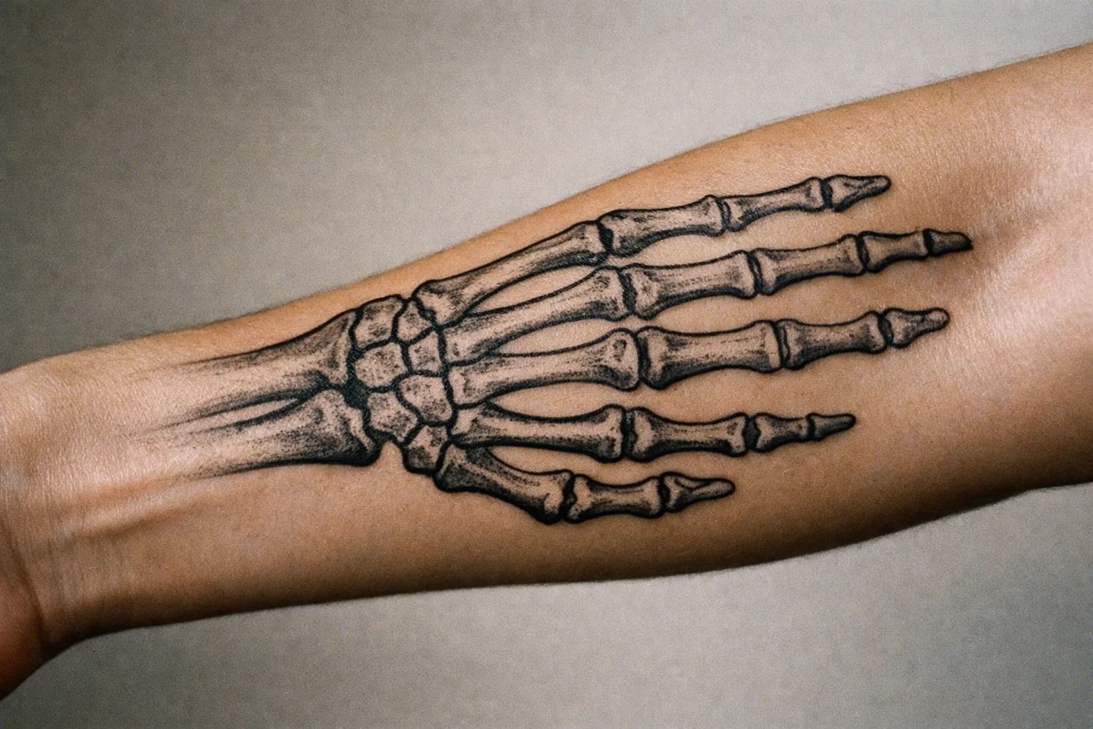 Close-up of a forearm skeleton hand tattoo with hyper-realistic shading and bone detail