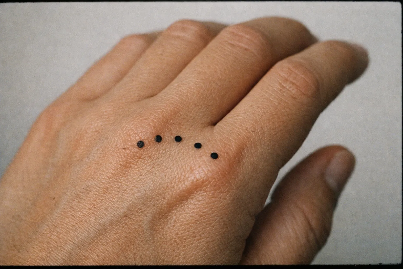 Back of a hand featuring five small dot tattoos arranged along the back near the knuckles
