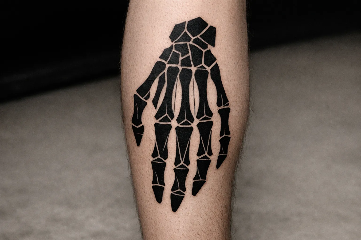 A black ink skeleton hand tattoo is shown on a person's leg.