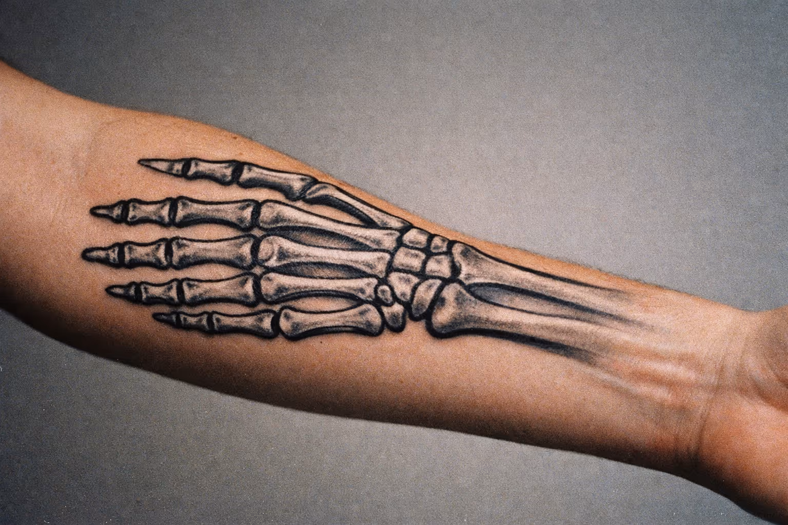 Lead editorial shot of a forearm with a skeleton hand tattoo, macro close-up showing crisp linework and realistic shading