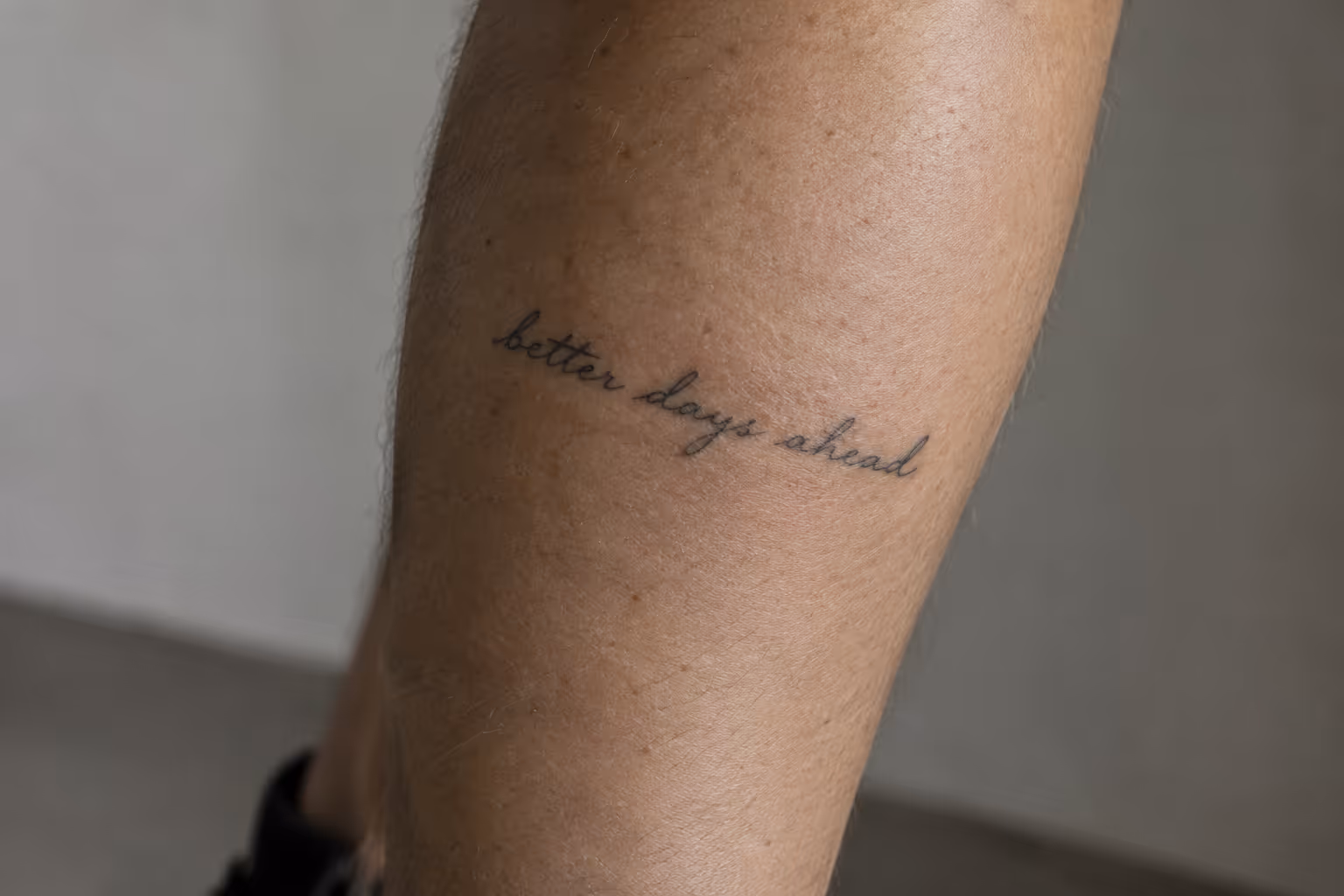 A person's lower leg bears a cursive 'better days ahead' tattoo.