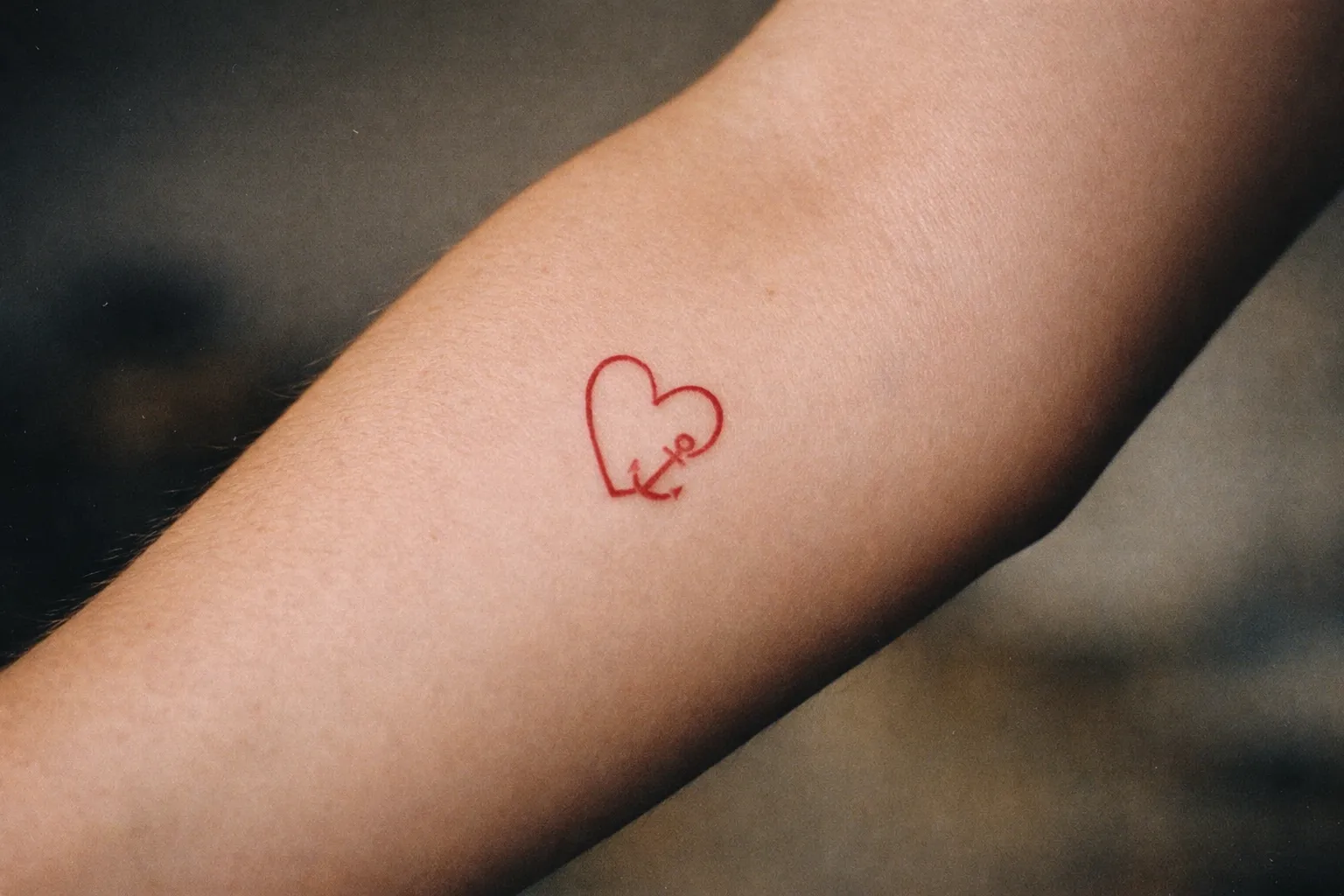 Close-up forearm heart tattoo with bold black linework and muted red fill, editorial close-up
