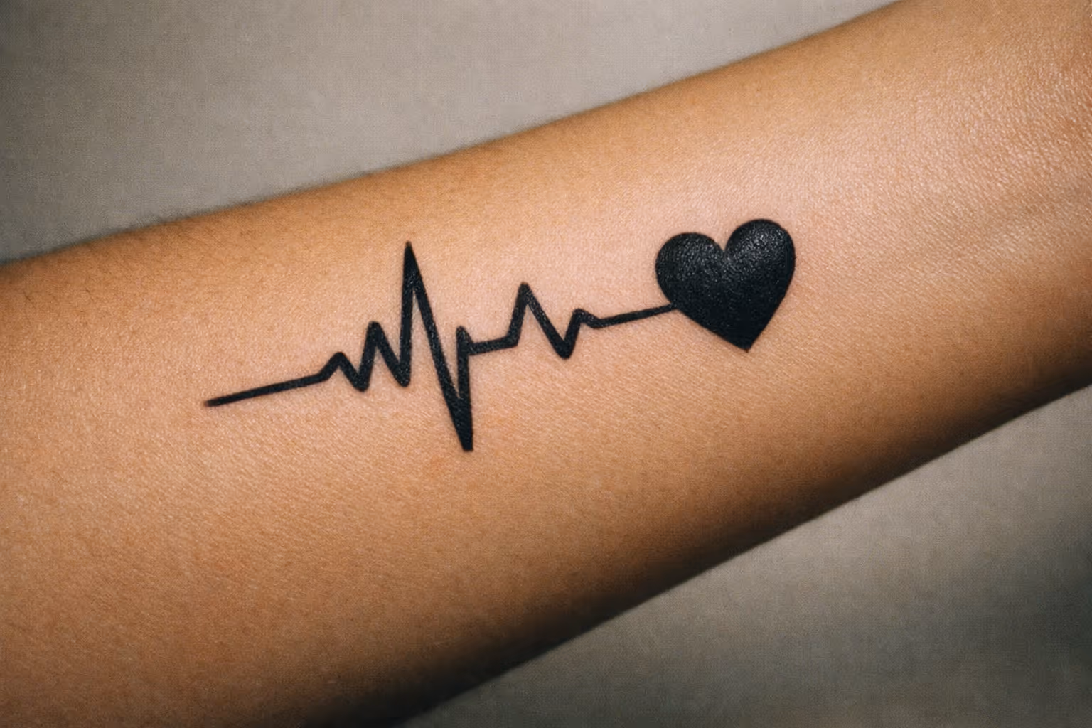 Editorial close-up of a heartbeat tattoo on forearm showing crisp black linework and a small heart at the end