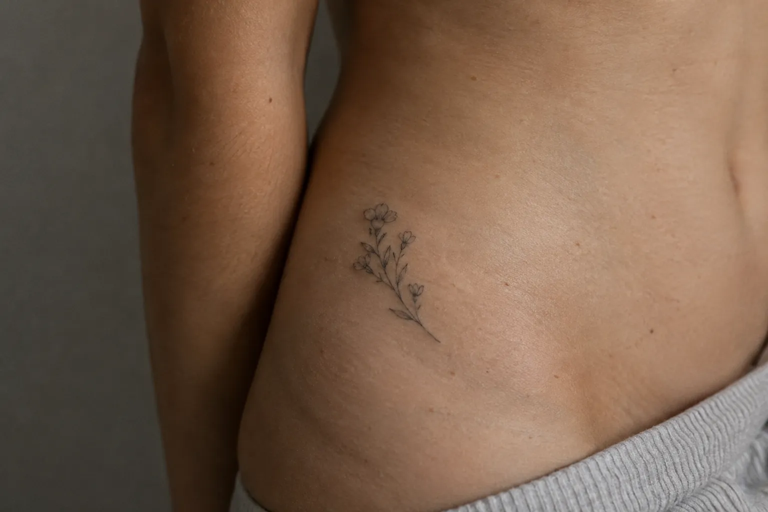 A small floral tattoo sits on a person's hip above the waistband of gray pants.