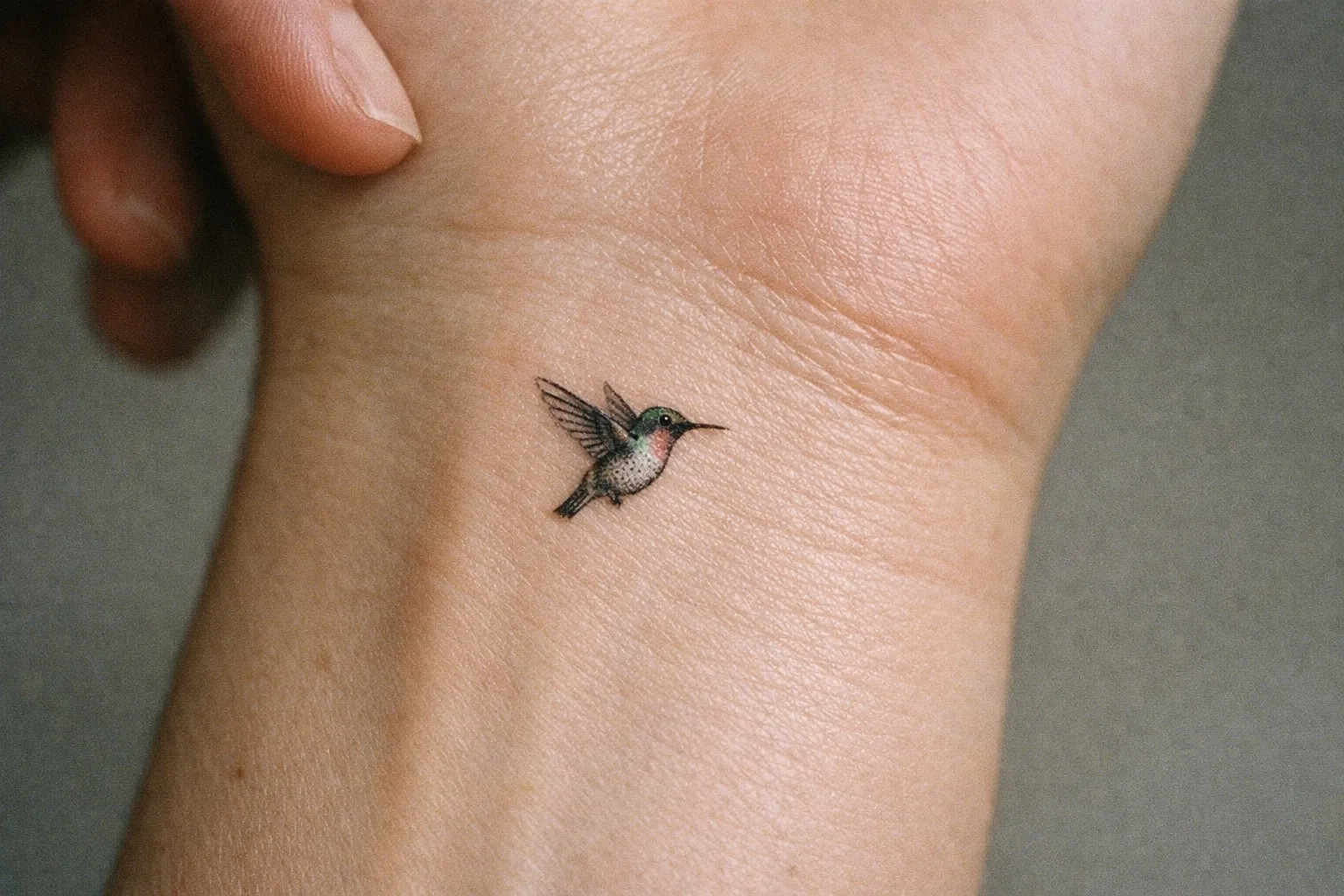 Tiny hummingbird tattoo on inner wrist shown in ultra-close macro.
