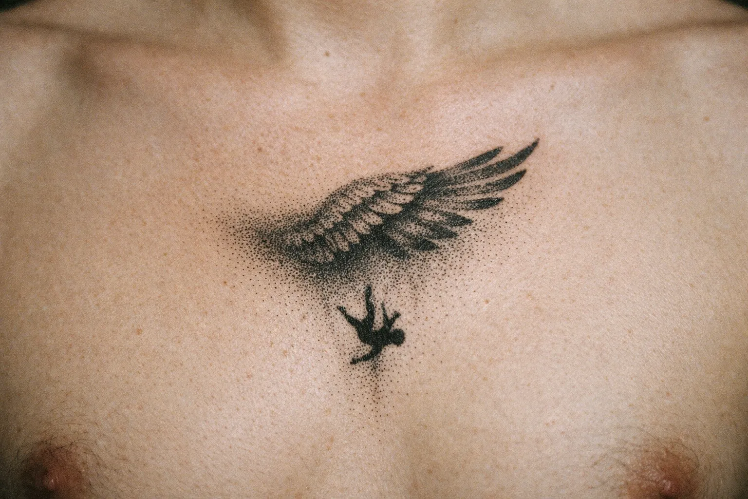 A tattoo of a wing and a falling figure is inked on a person's chest.