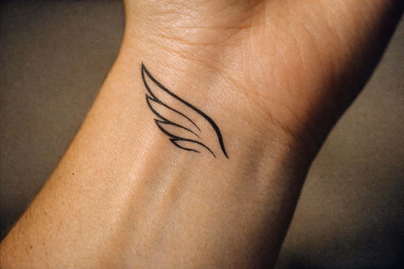 A minimalist wing tattoo on the inside of a person's wrist.