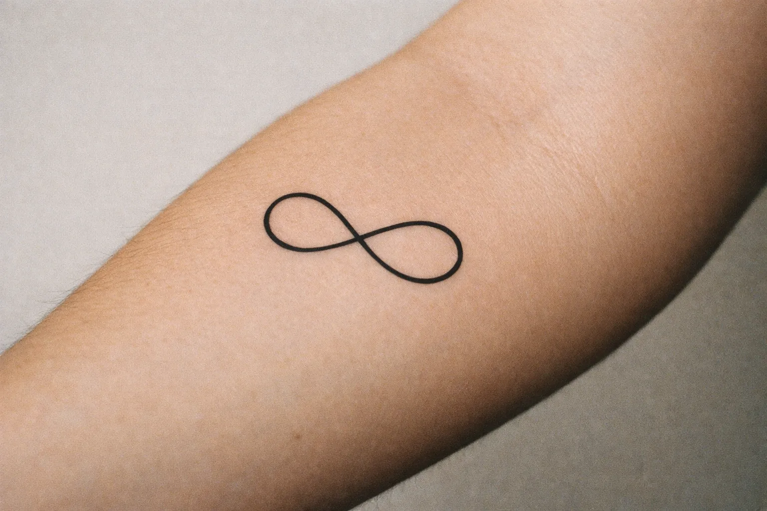Angled forearm shot featuring a minimalist infinity tattoo with clean lines