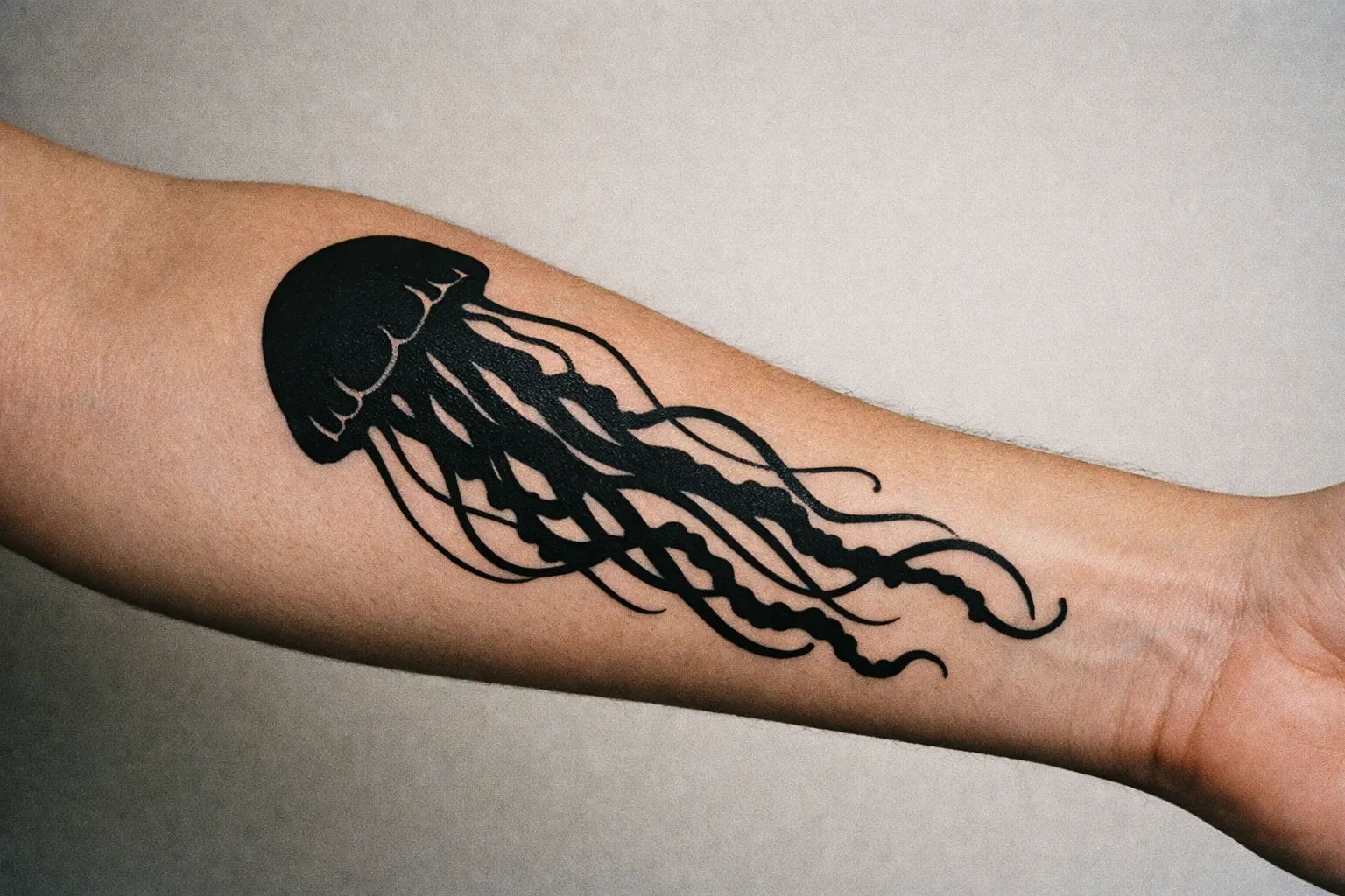 Bold black jellyfish silhouette tattoo on forearm with curling tentacles