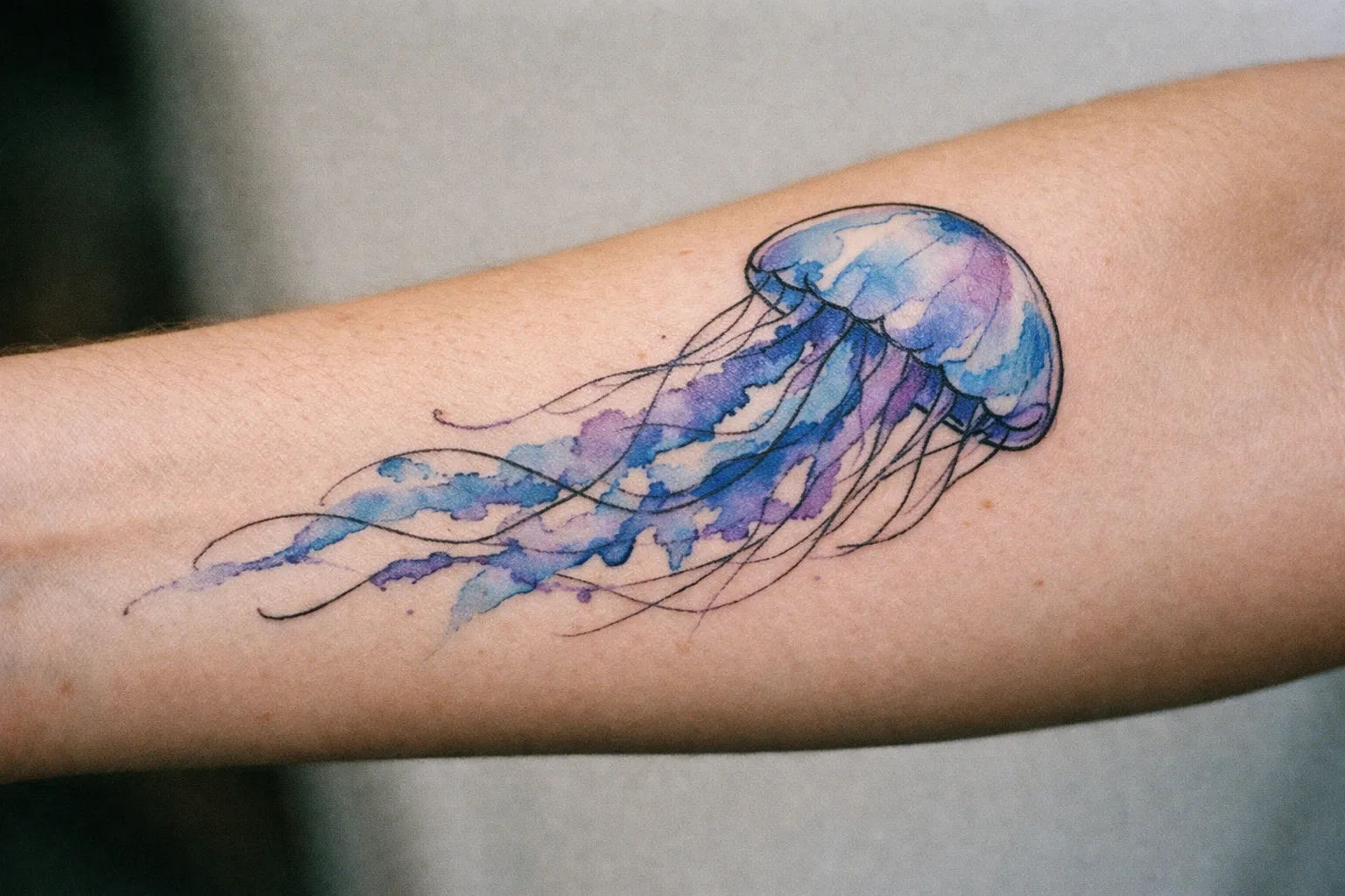Watercolor jellyfish tattoo on forearm with blue and purple ink washes