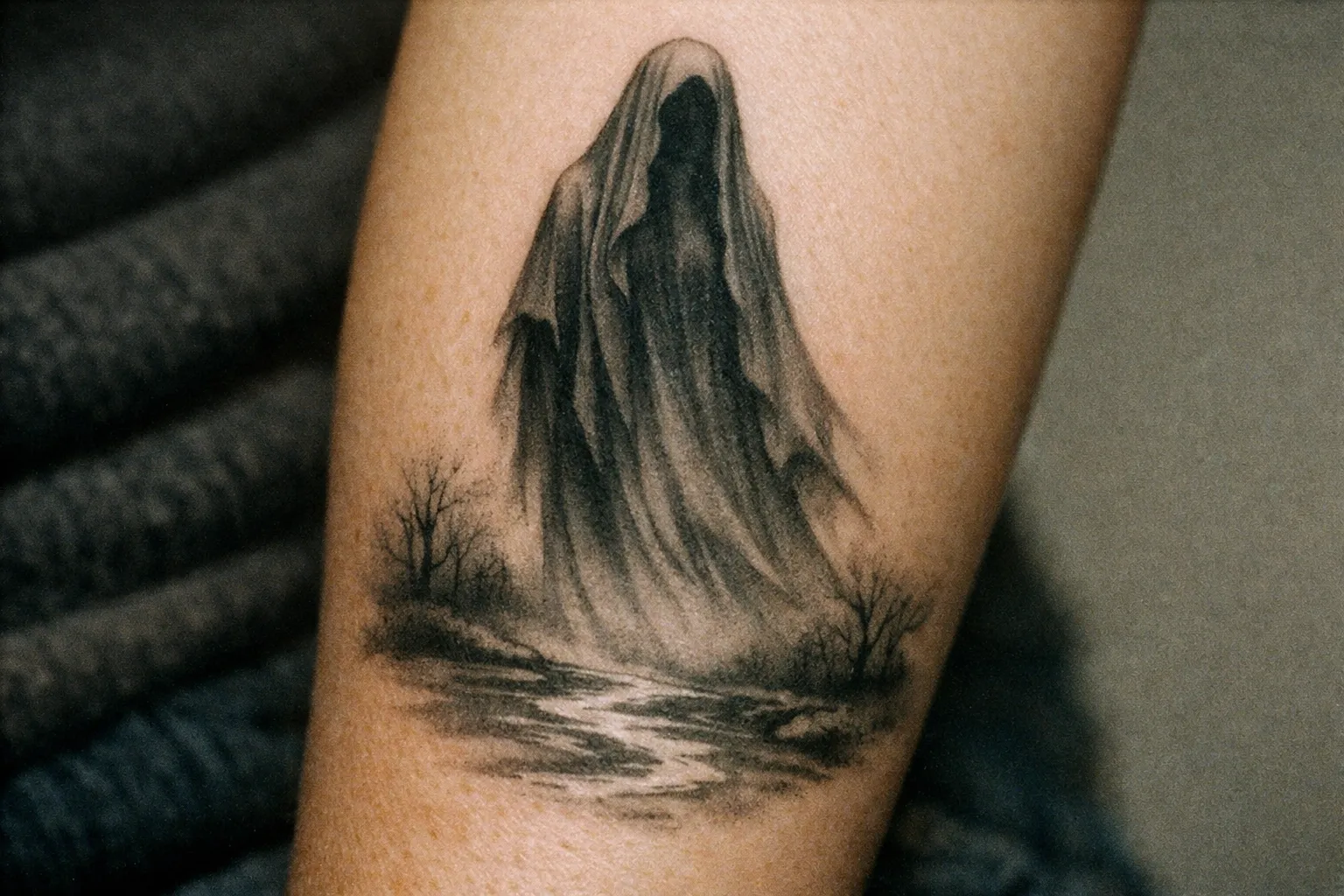 Close-up La Llorona tattoo on forearm with veiled figure and river motif.