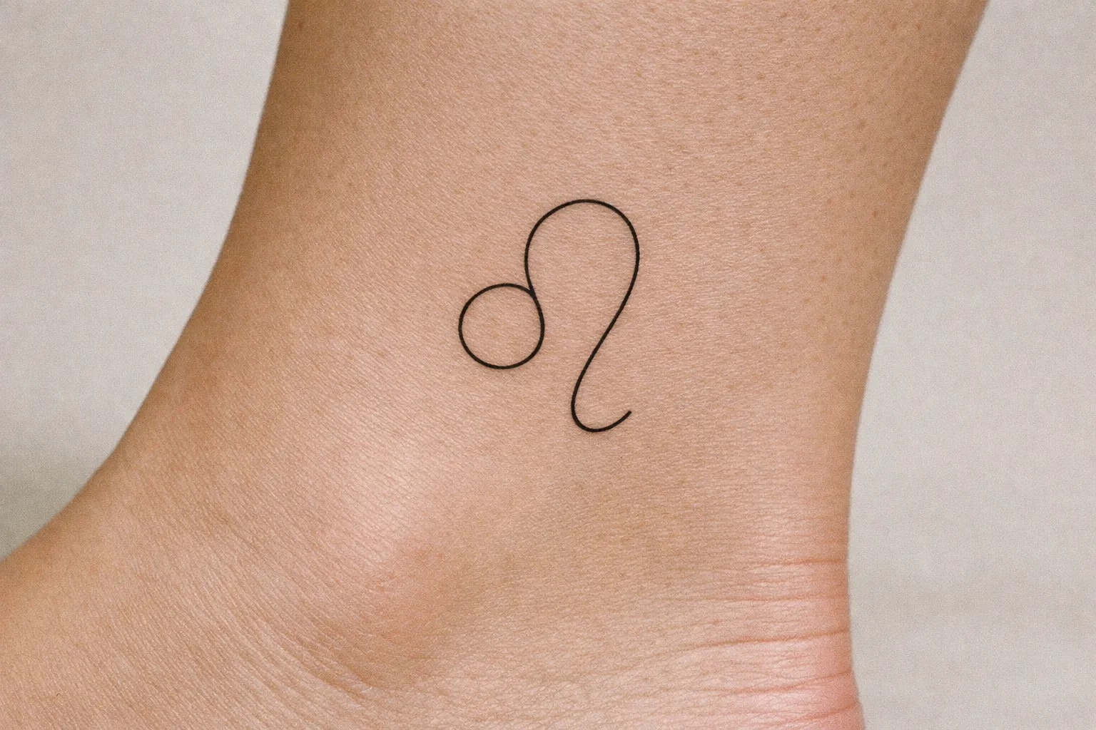 A simple Leo zodiac symbol tattoo on the side of a person's ankle.