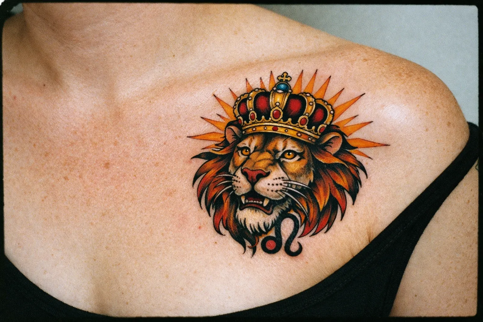 A person displays a colorful lion head with crown and Leo symbol tattooed on their upper chest.