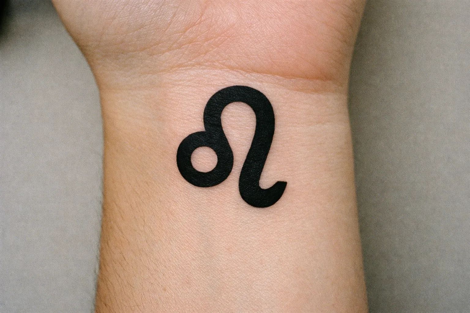 A Leo zodiac symbol tattoo is inked on the inner wrist of a person.