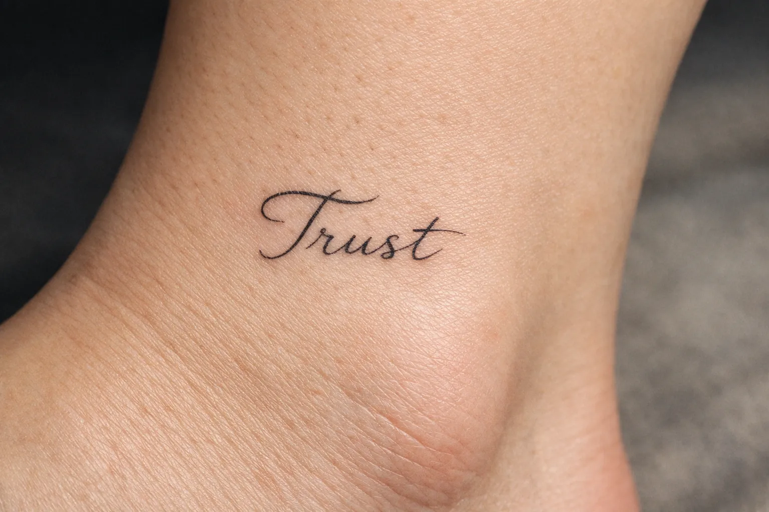 A cursive Trust tattoo on a person's ankle.