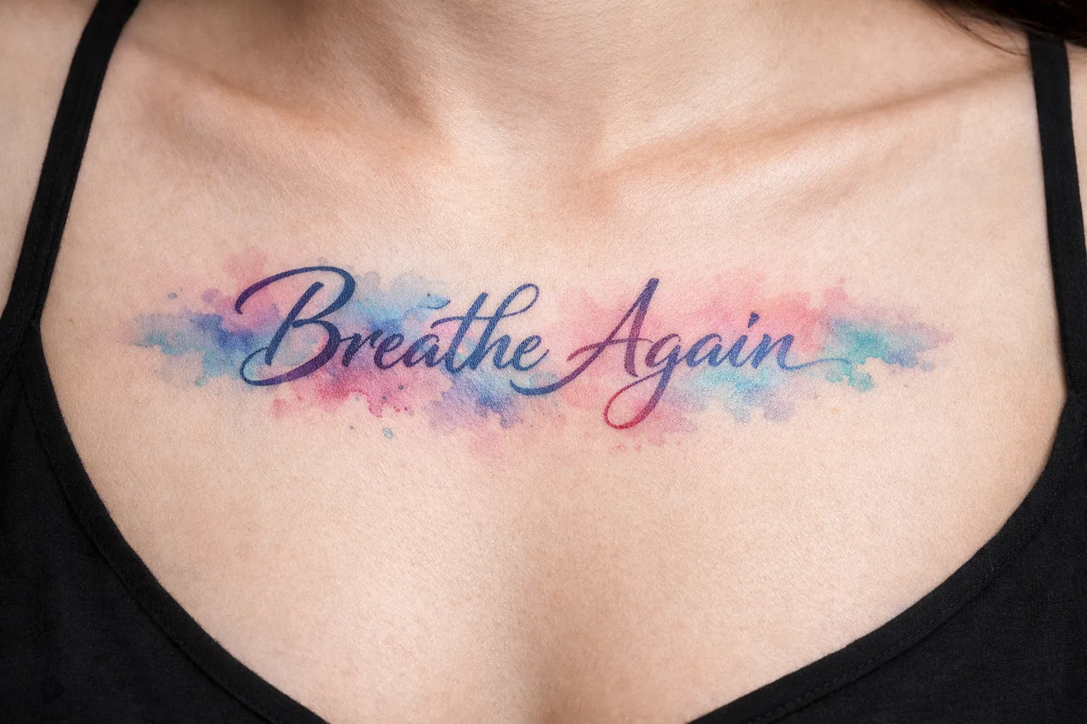 A person with a 'Breathe Again' script tattoo across the upper chest over a watercolor background.