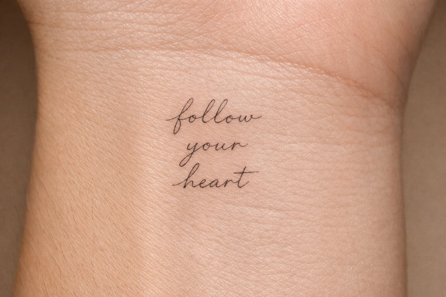 Wrist with a cursive 'follow your heart' lettering tattoo.