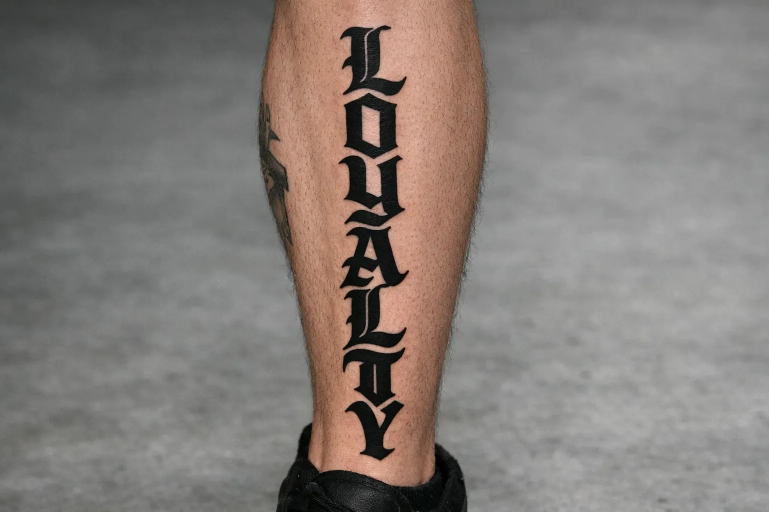 A person's lower leg with a bold black tattoo of the word 'LOYALTY' in large script.