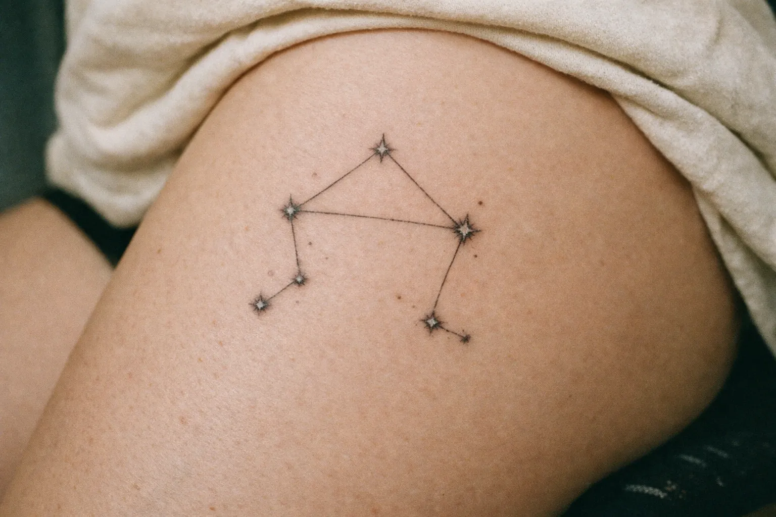A Libra constellation tattoo is inked on a person's upper thigh.