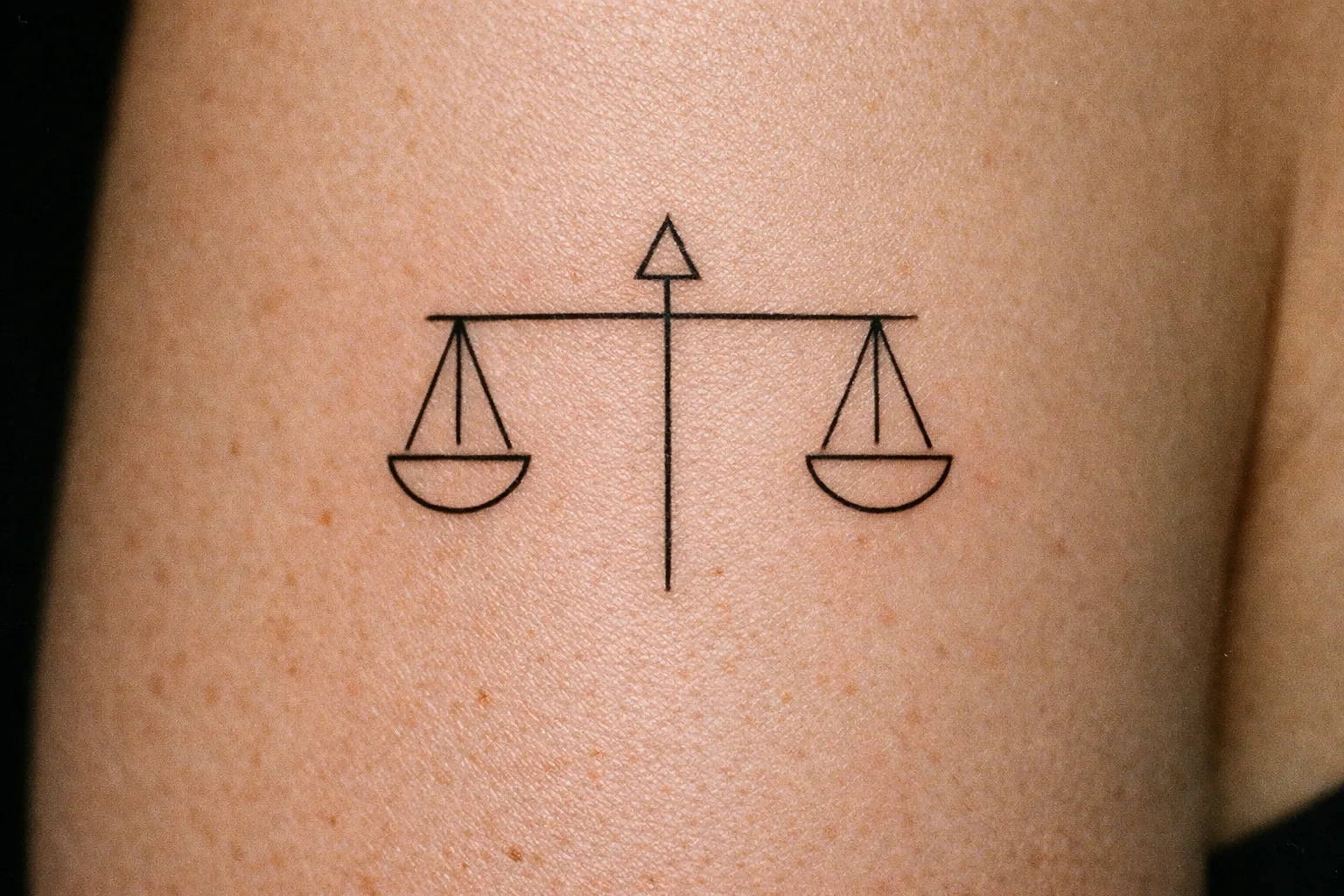 A simple scales of justice tattoo is inked on a person's arm.
