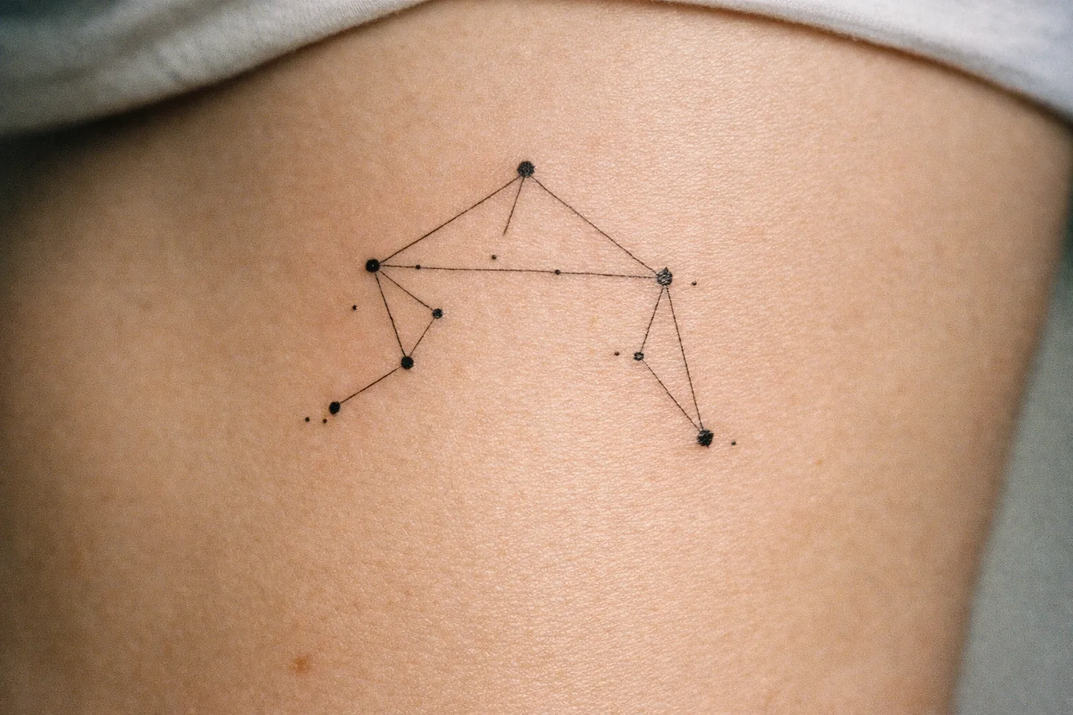 A minimalist Libra constellation tattoo is inked on a person's upper thigh.