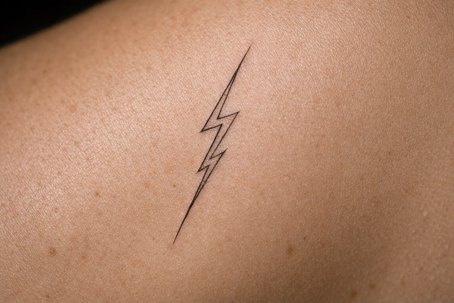 A simple lightning bolt tattoo on a person's shoulder.