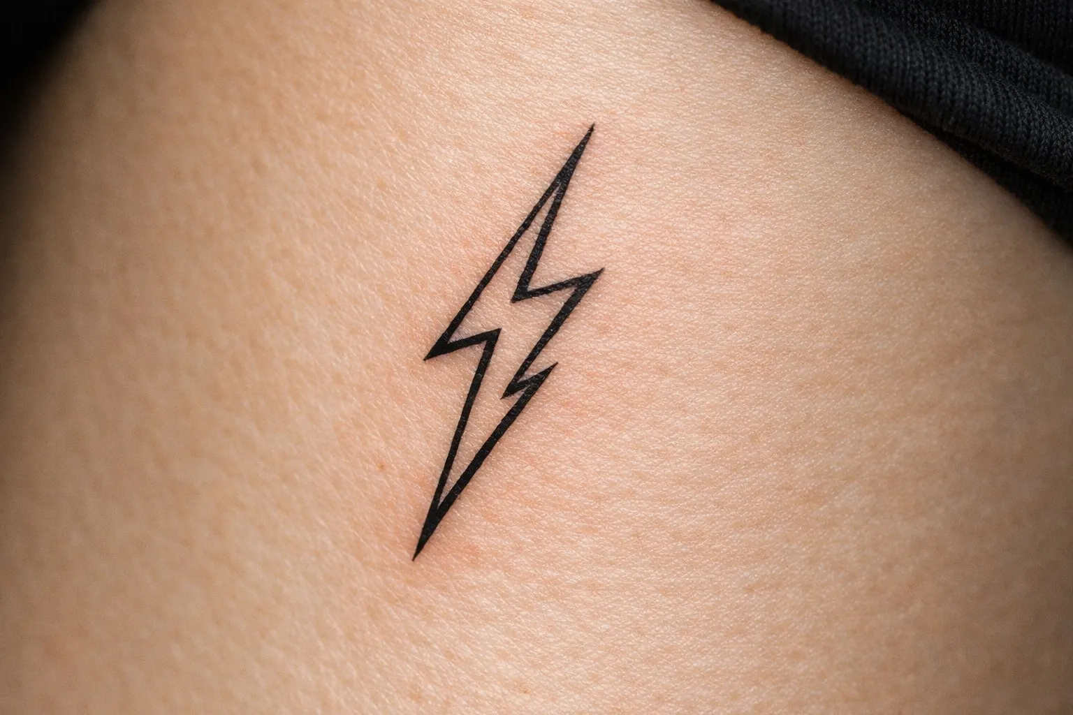 A simple black lightning bolt tattoo on light skin.