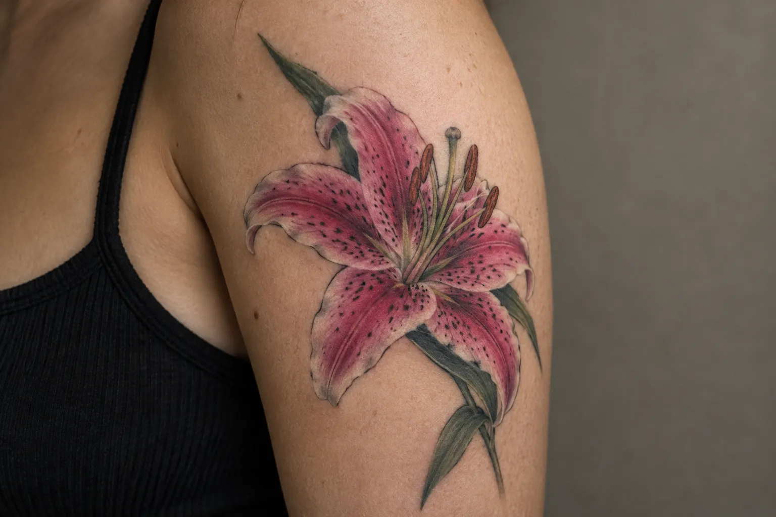 Healed color stargazer lily tattoo on the outer upper arm, hot pink petals fading to white with dark spots