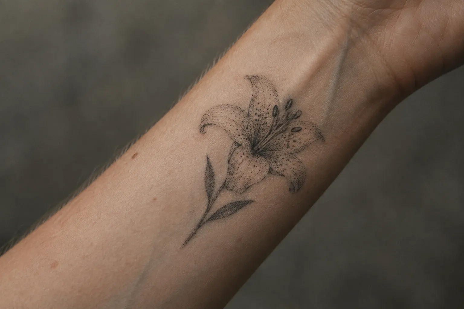 A dotwork lily tattoo with speckled petals sits on a person's inner wrist.