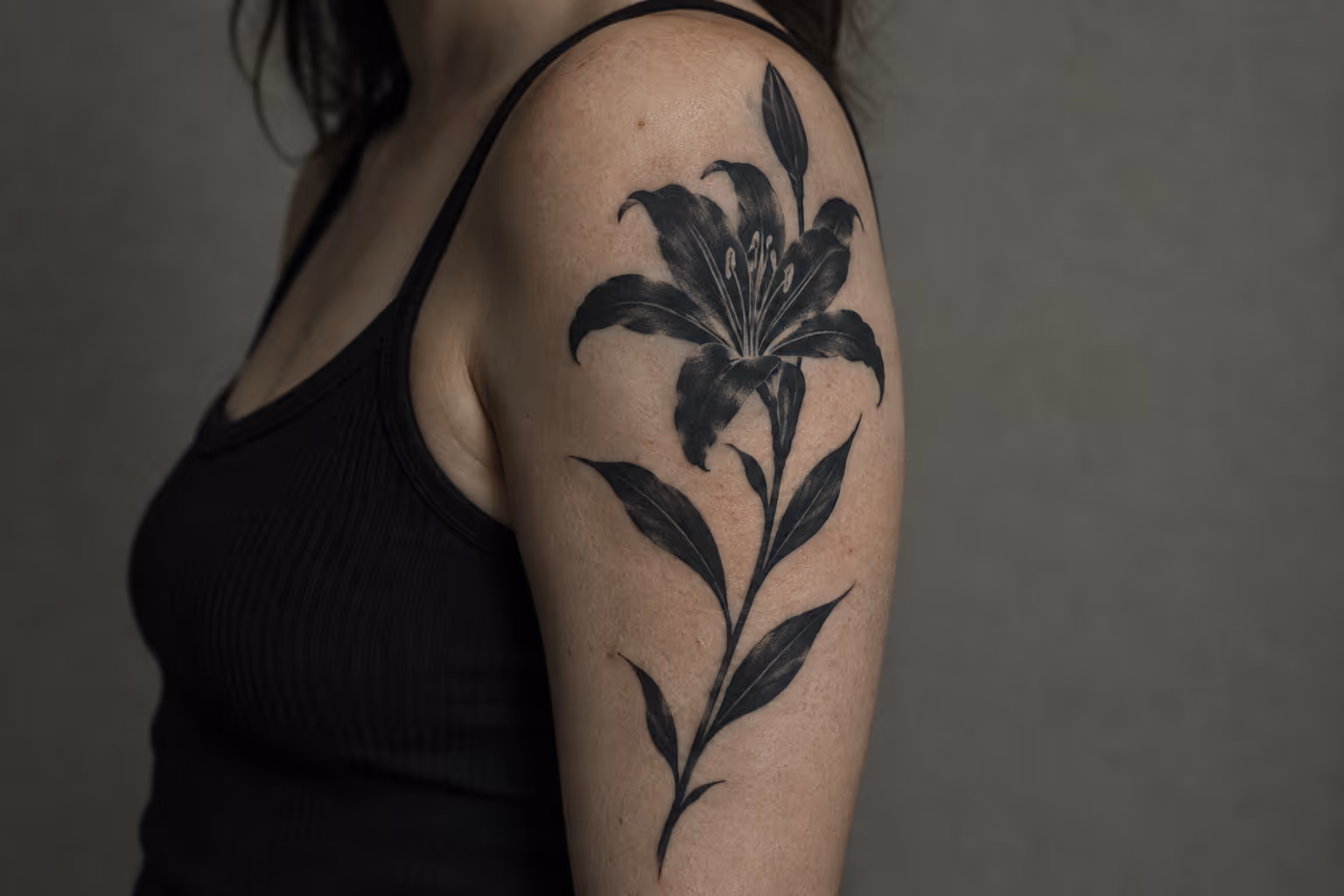 A person in a black top has a large black lily tattoo on their upper arm.