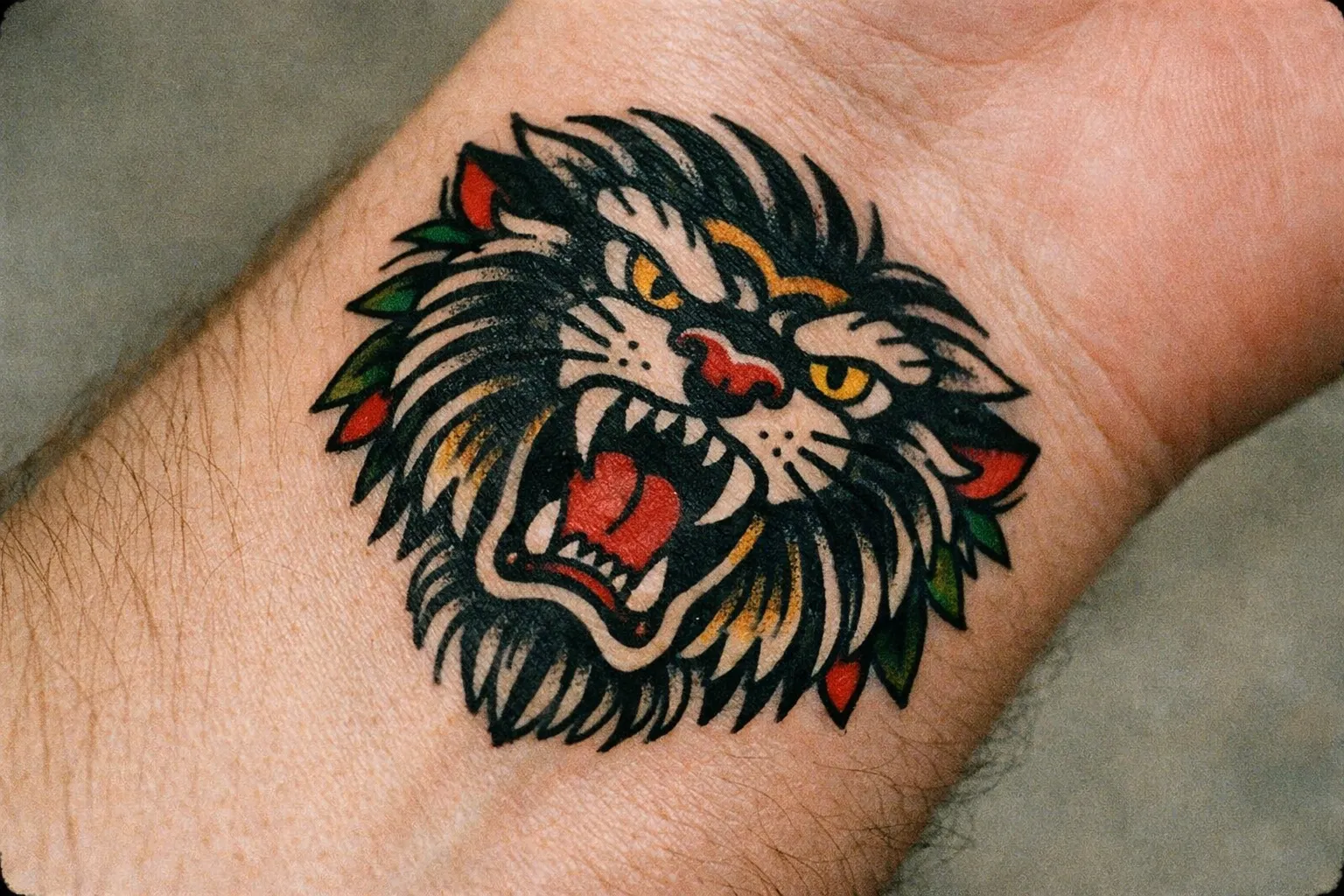 A colorful roaring lion head tattoo on a person's wrist.