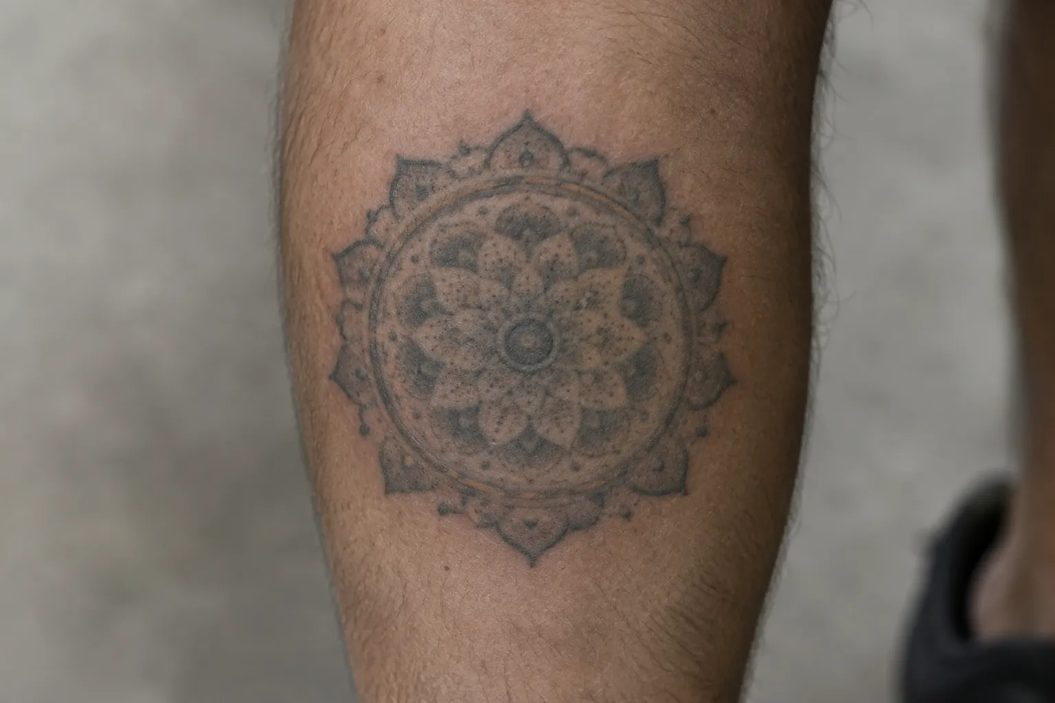 A healed dotwork mandala tattoo on a person's lower leg, its fine dots softened with age.