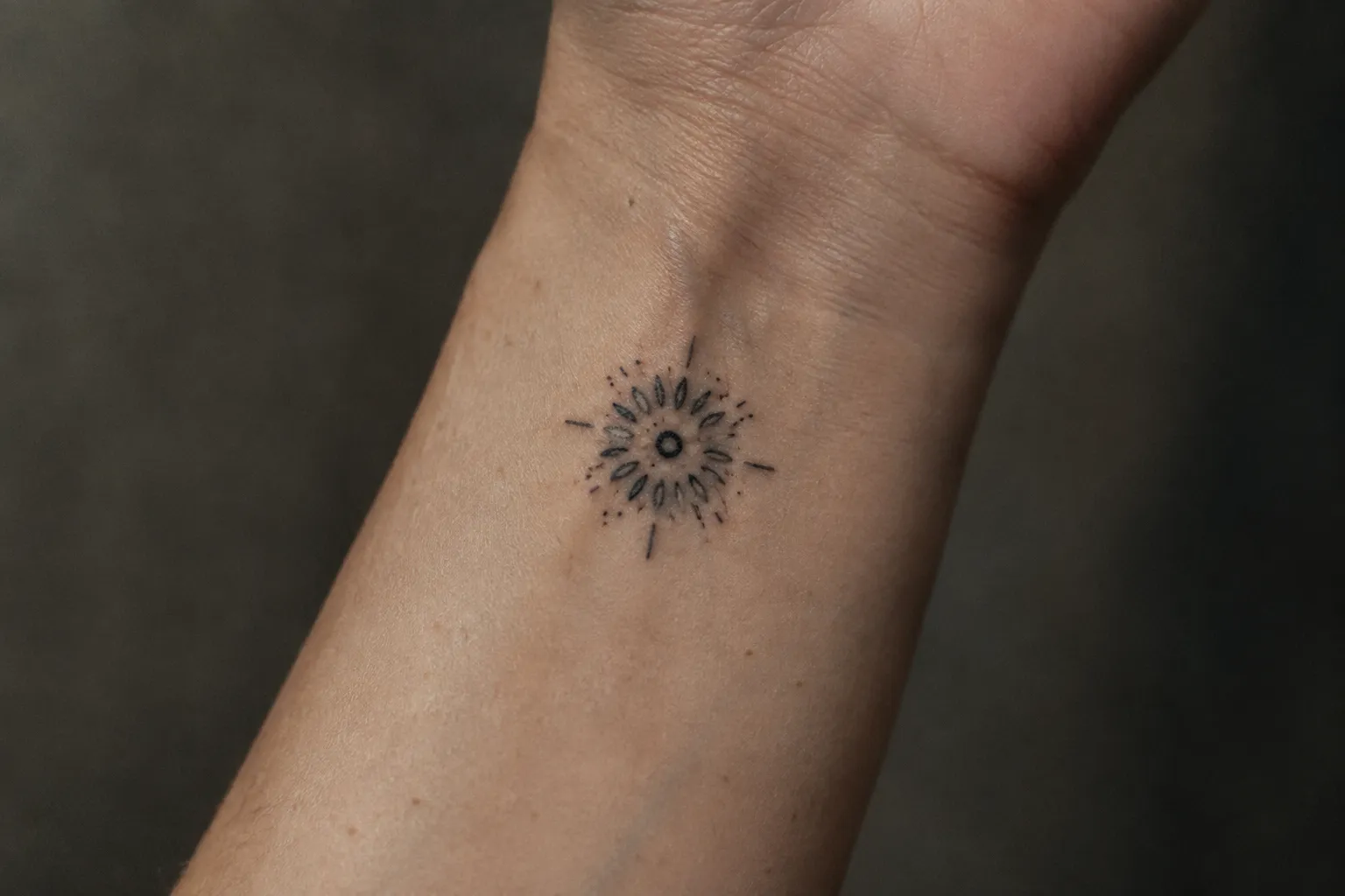 A small black mandala tattoo sits on the inner wrist of an arm.