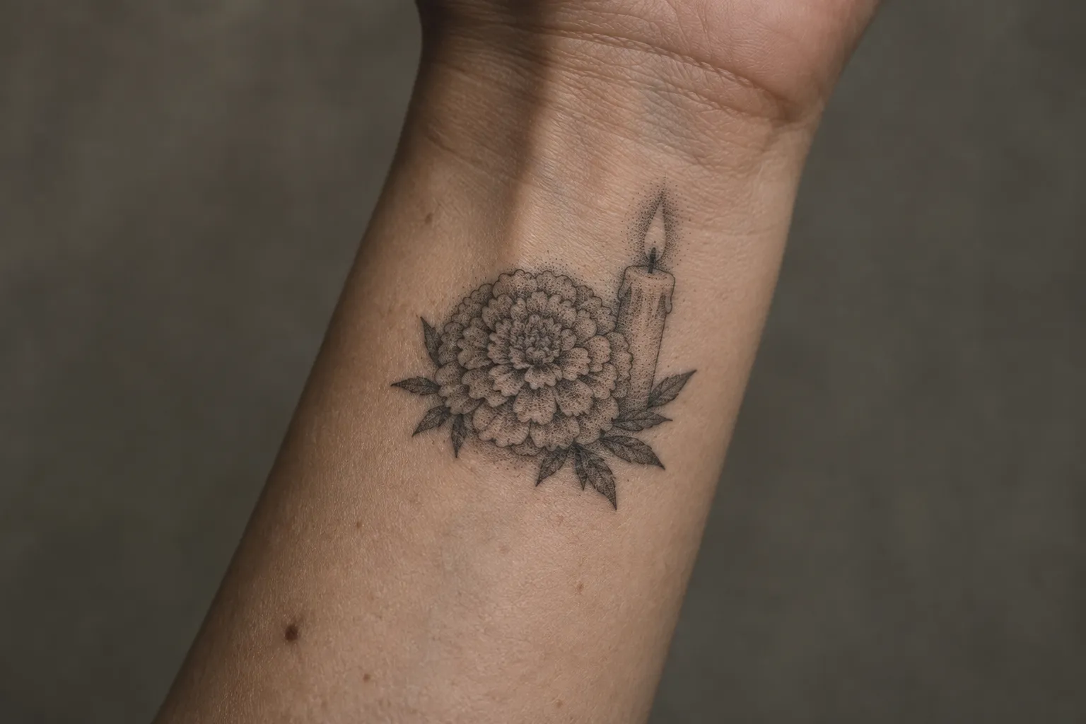 A dotwork marigold and lit candle tattoo on a person's inner wrist.