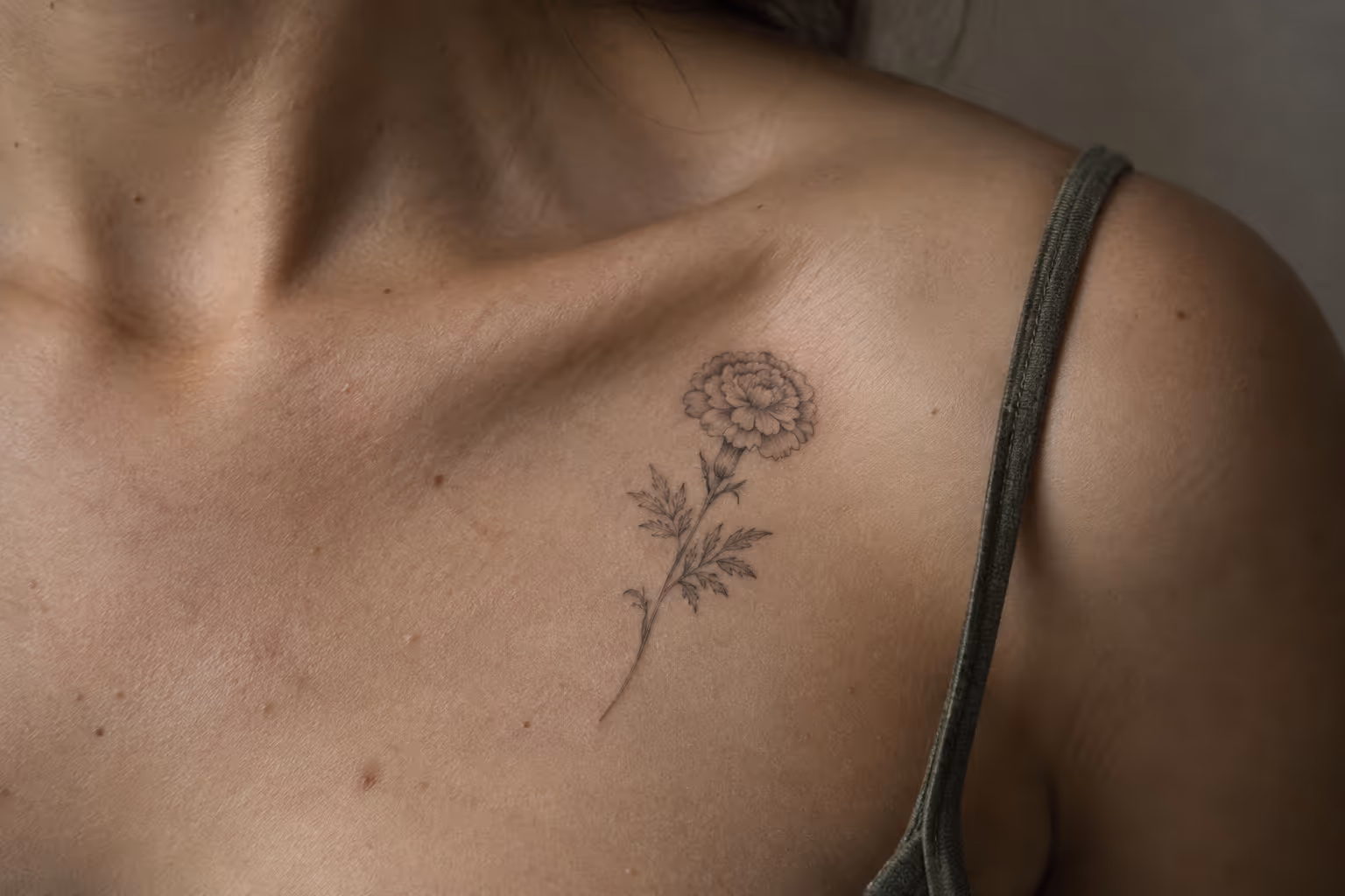 A person has a fine-line marigold tattoo on the upper chest near the shoulder.