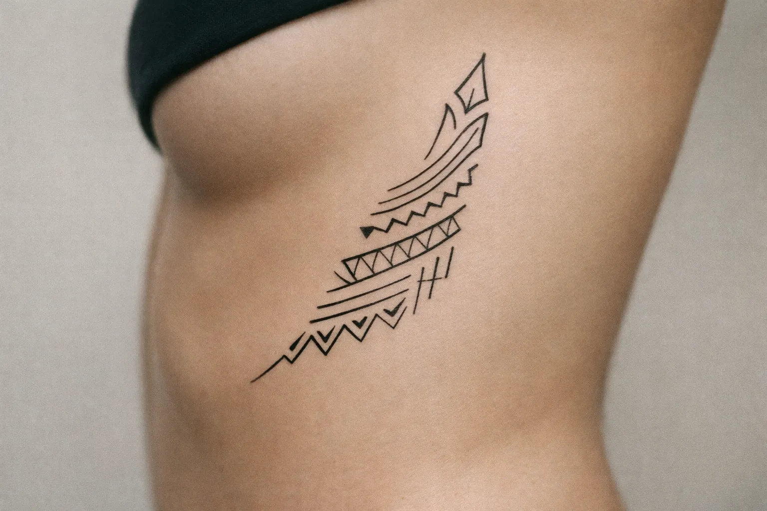 A person's side torso with a geometric black tattoo featuring Marquesan-inspired patterns.