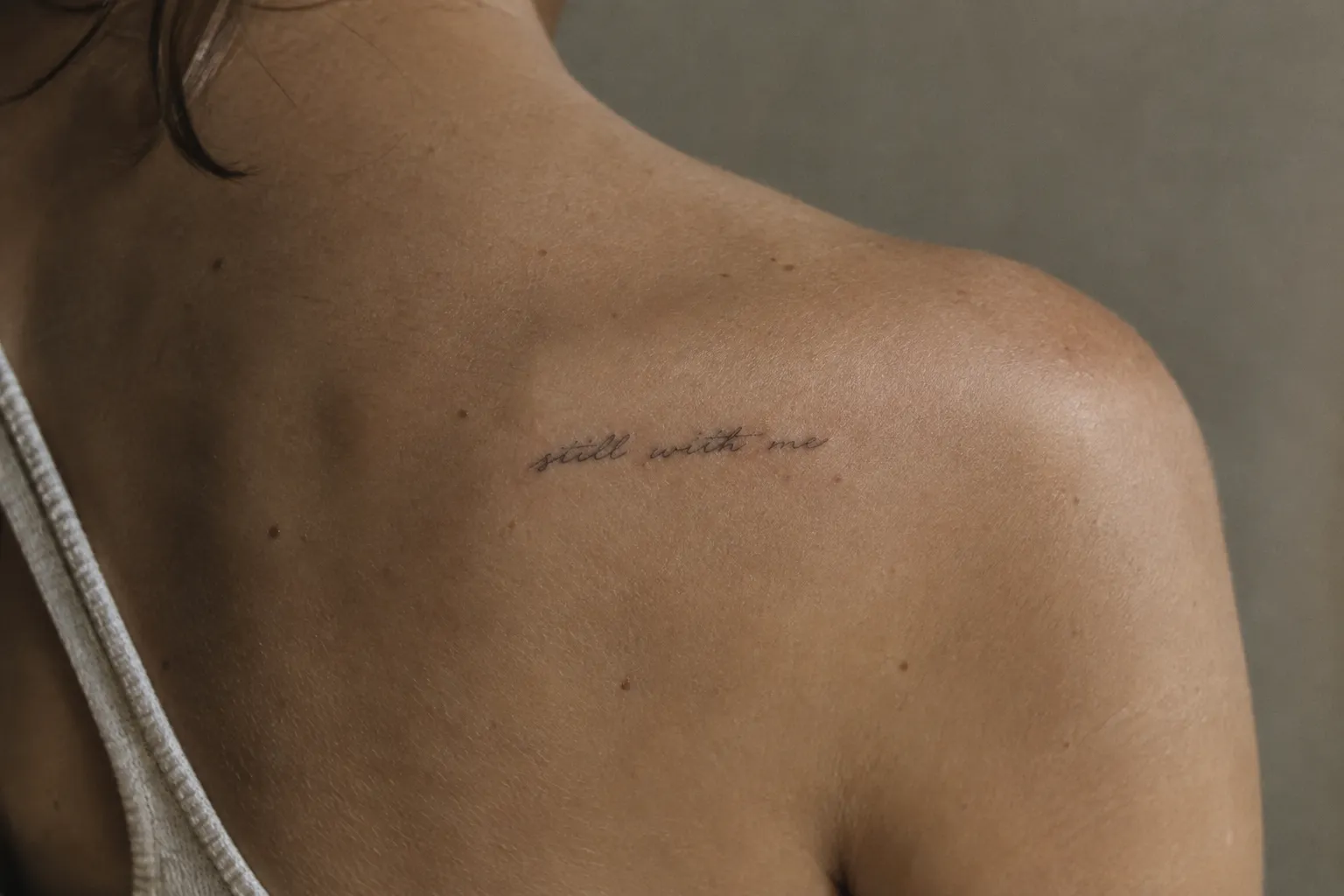 A person's shoulder bears the memorial tattoo 'still with me.'