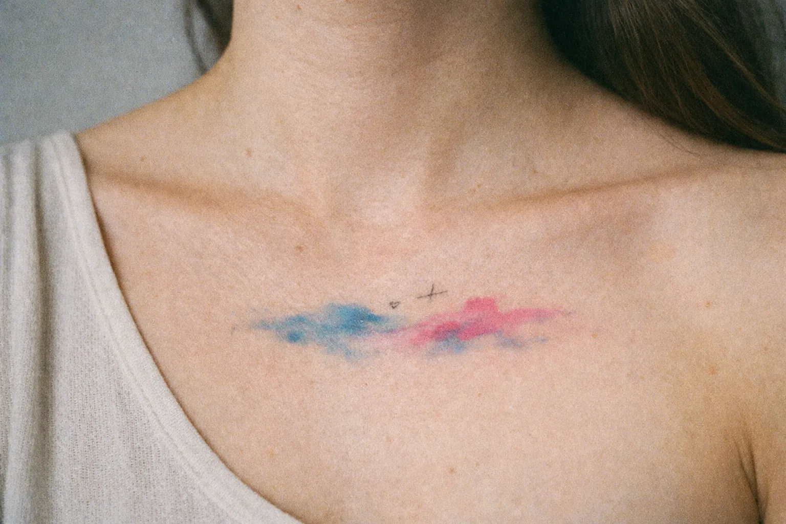 A person with a blue and pink watercolor tattoo on their upper chest near the collarbone.